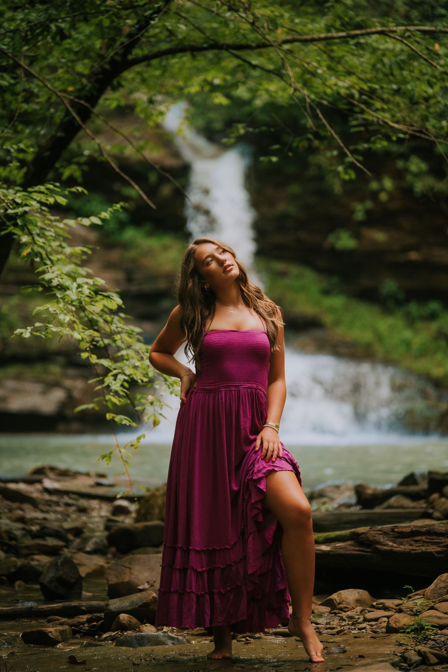 A scenic waterfall forms the backdrop for an artistic portrait in a burgundy dress.