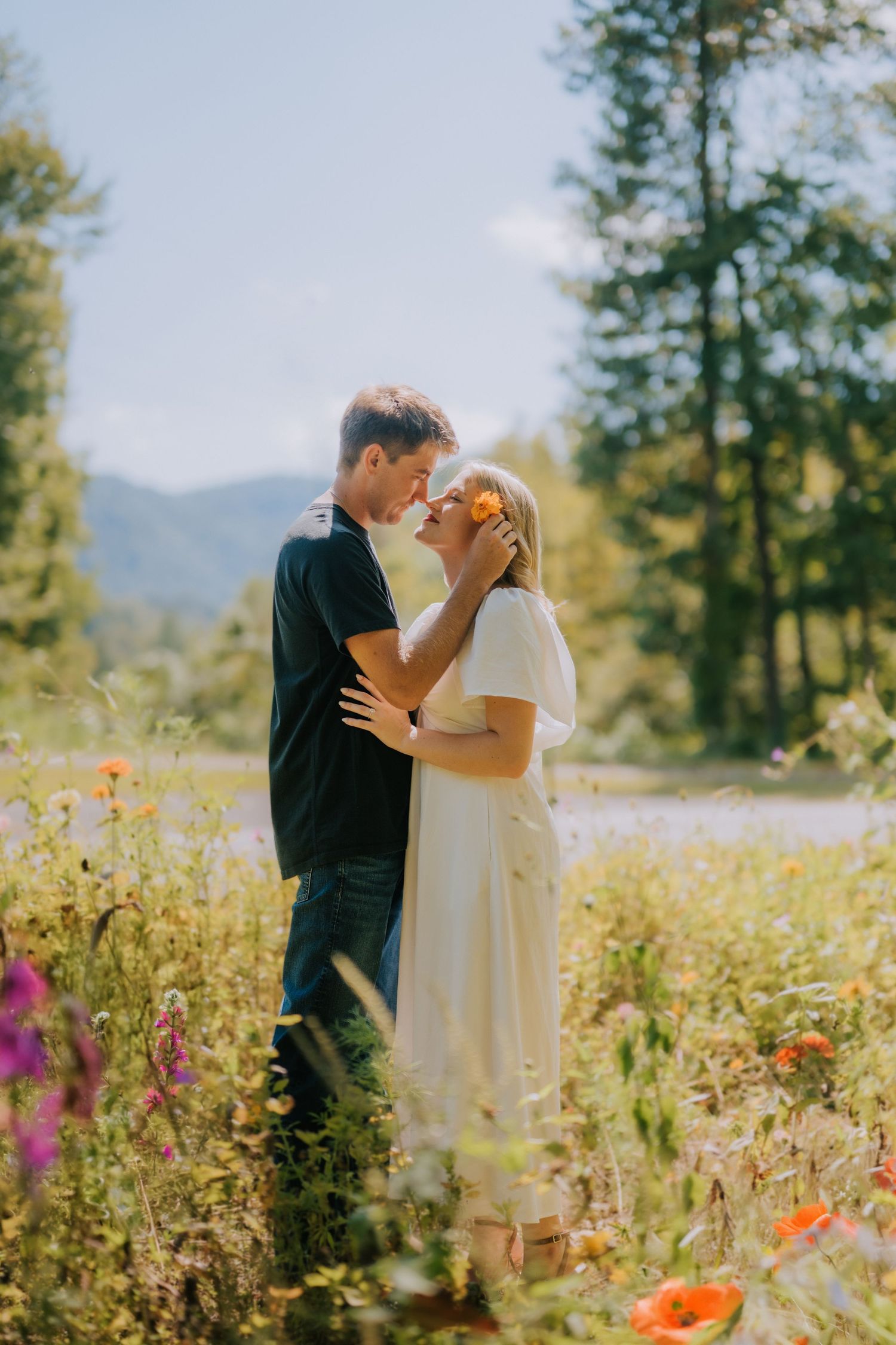 Intimate moment shared in wildflower field with mountains and forest in background.