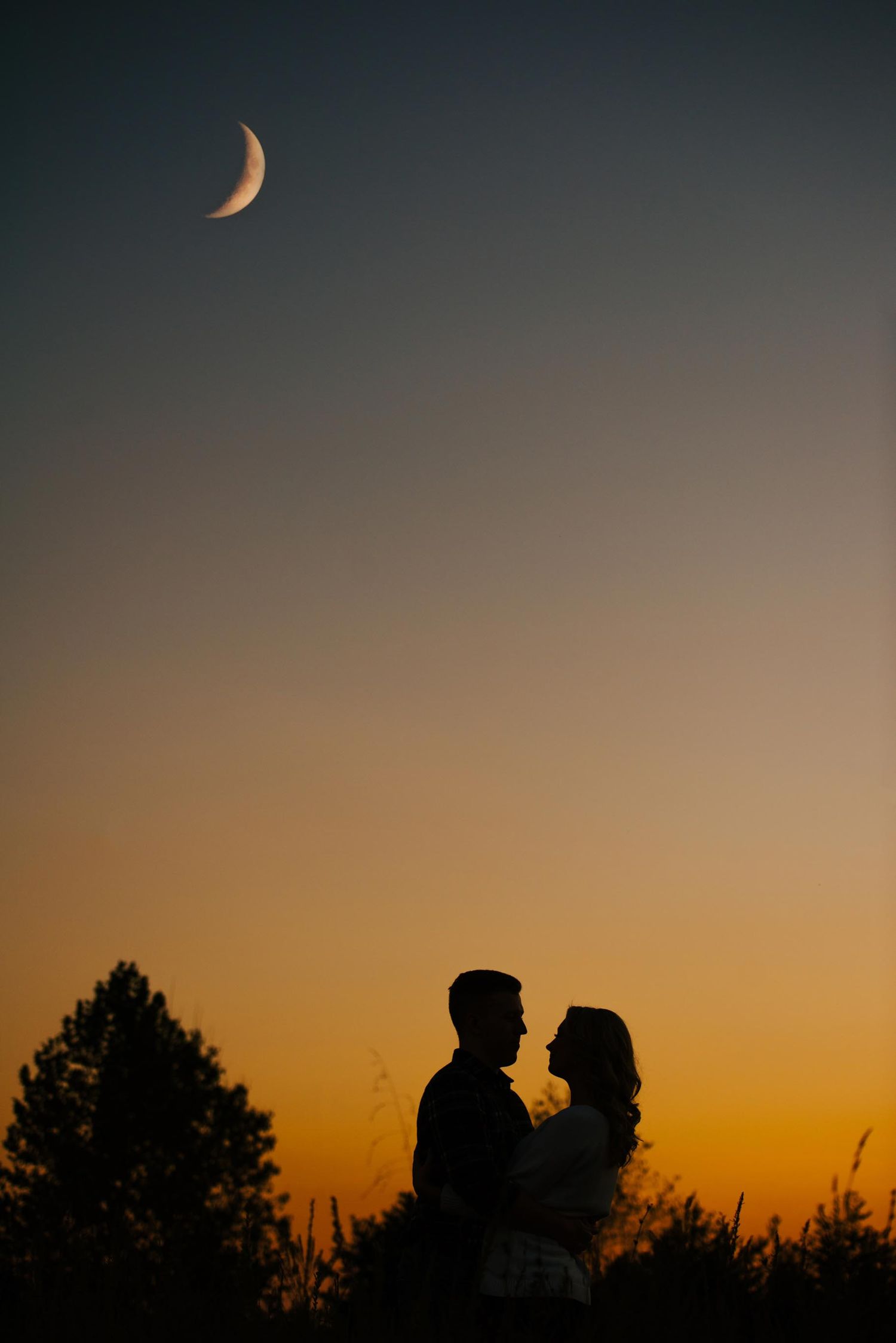 Silhouetted figures against a dramatic sunset sky with crescent moon.