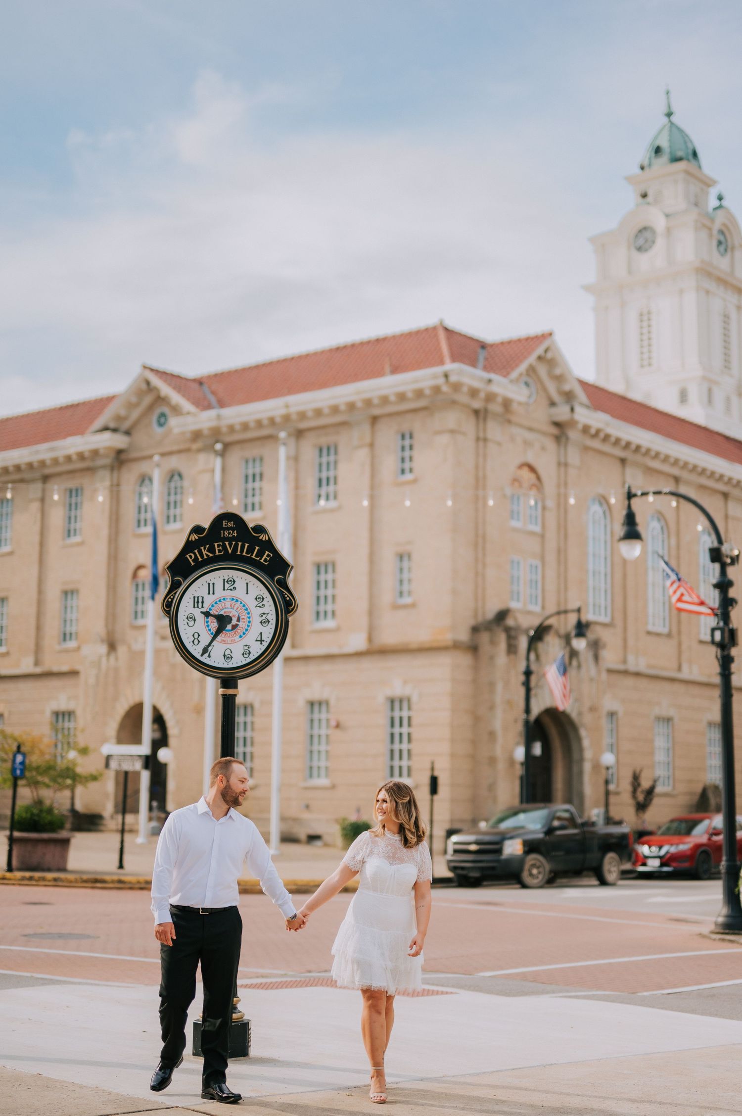 A couple strolls hand in hand past a beautiful historic courthouse building on a sunny day.