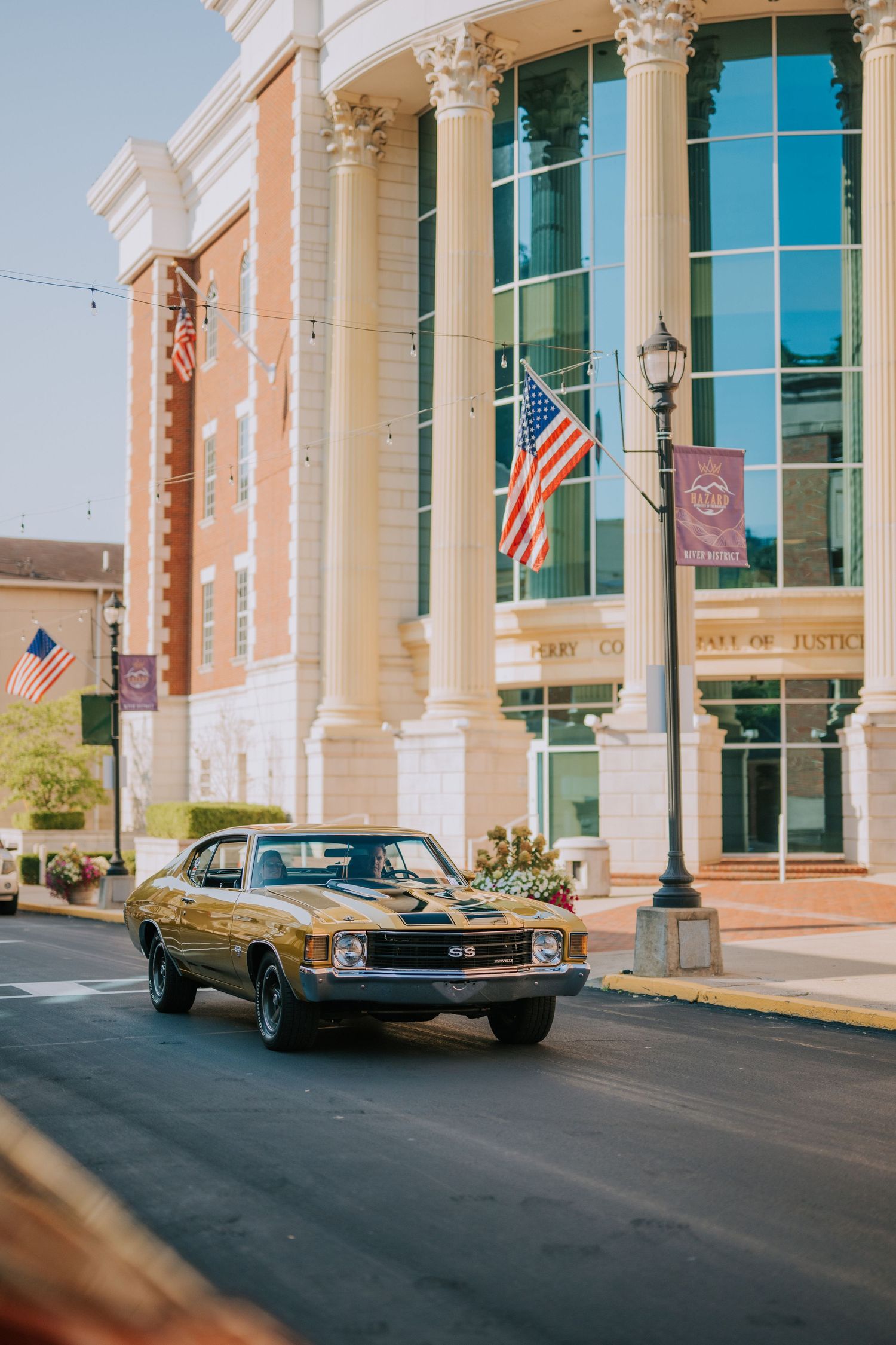 A classic vintage car parked in front of a modern building with American flags.
