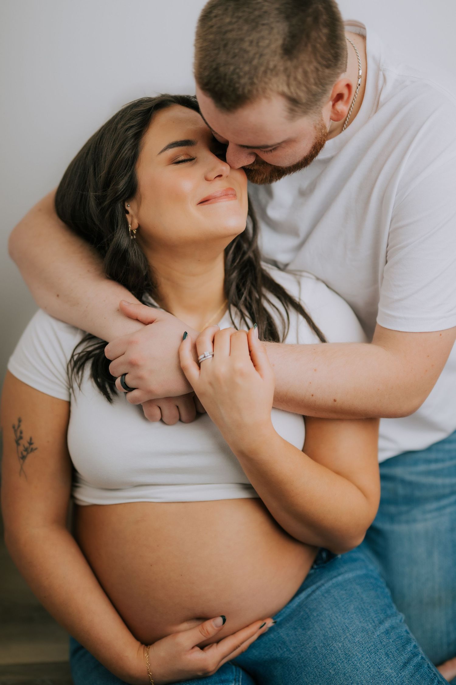 Intimate maternity photo showing a tender embrace between couple in white shirts with visible baby bump.