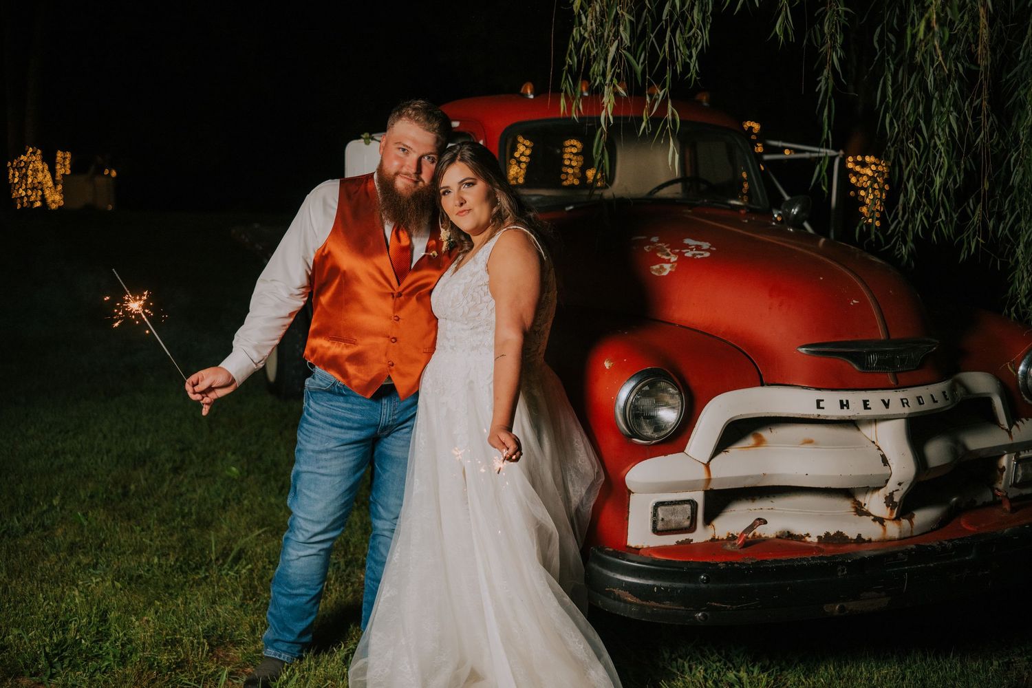 Wedding couple poses with vintage red truck during sunset photo session.
