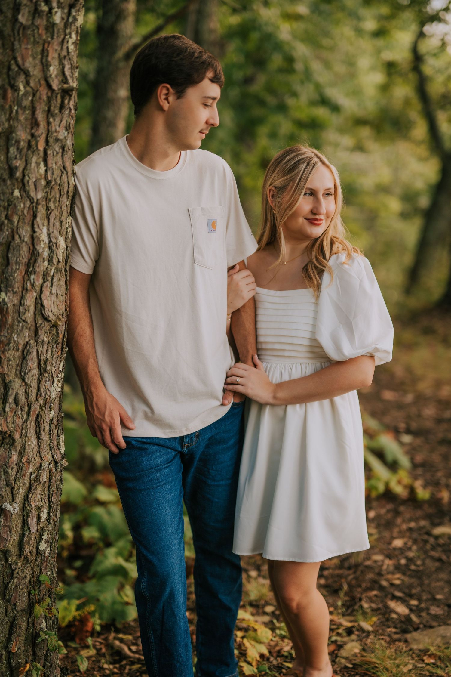 A couple in casual white outfits embracing among trees in a romantic woodland photoshoot.