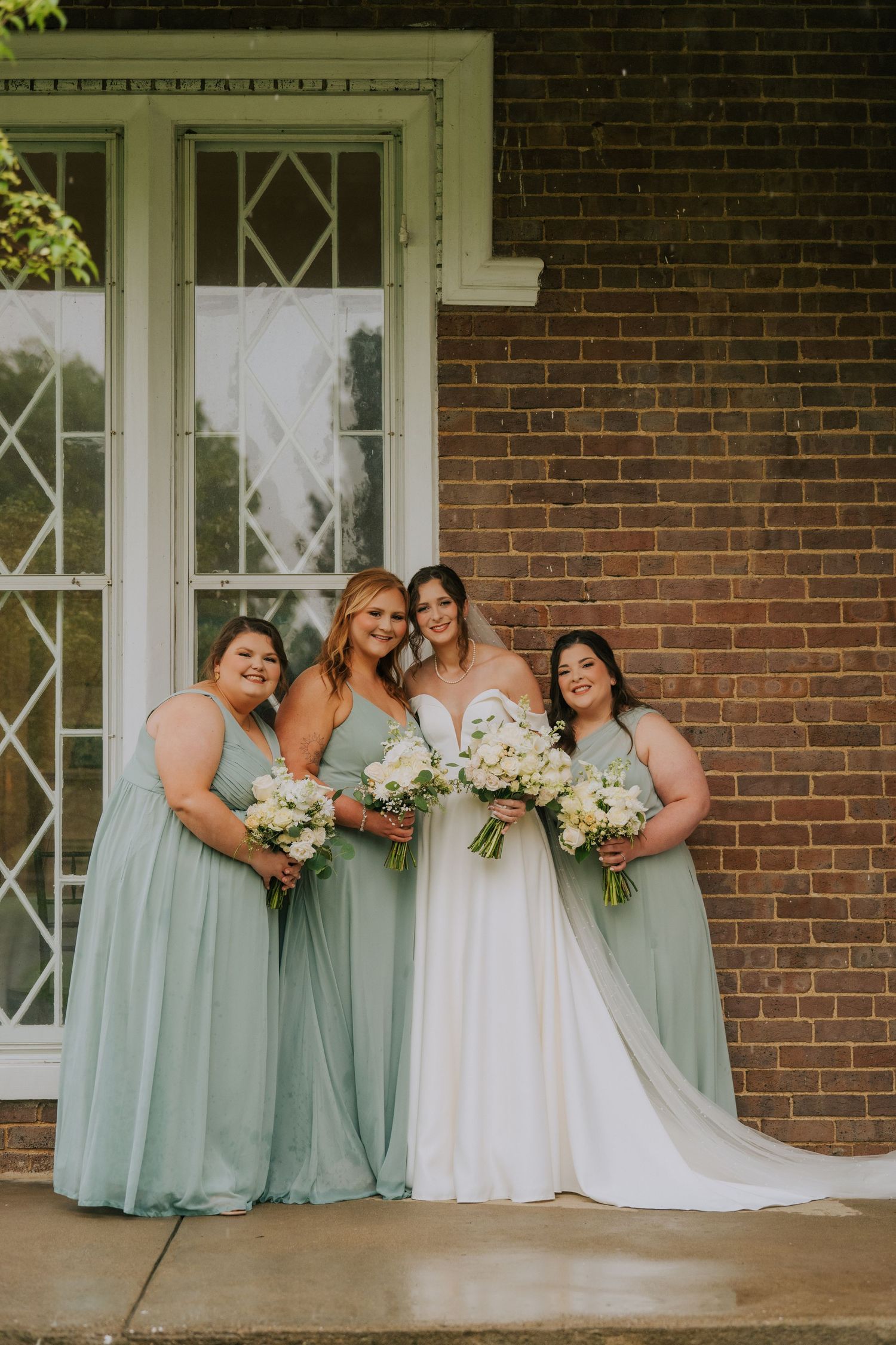 Bridesmaids in mint green dresses gather for photos on a brick porch.