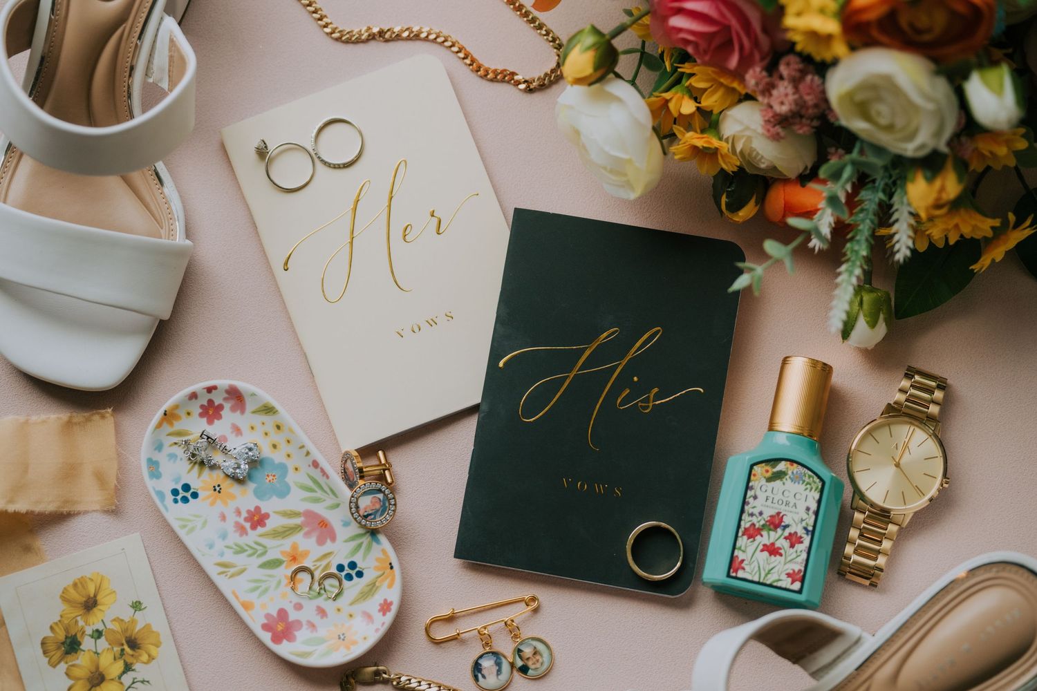 Wedding details flat lay with rings, invitations, and fresh flowers in pastel colors.