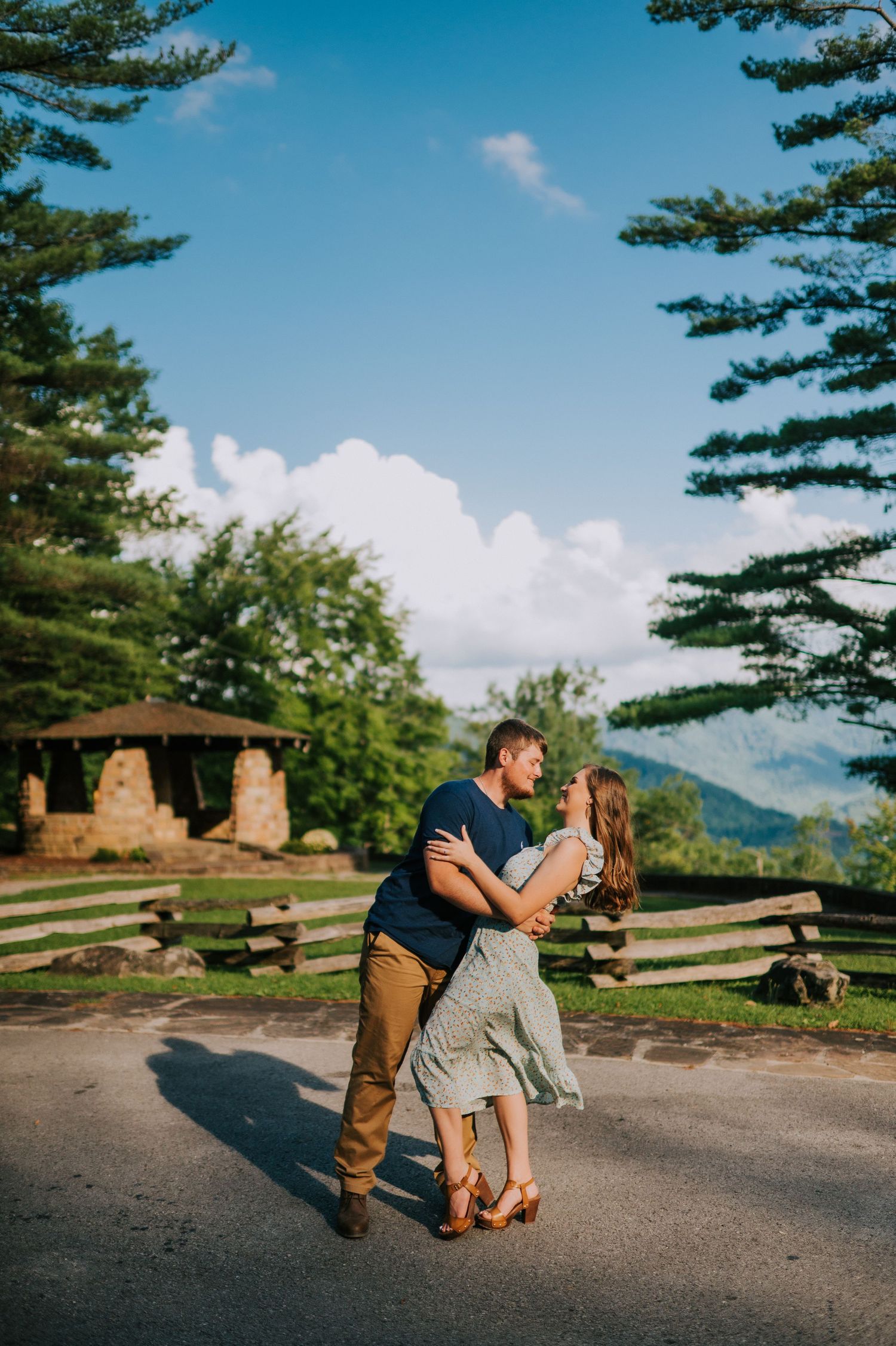A romantic dip pose against a scenic mountain backdrop with blue skies and pine trees.