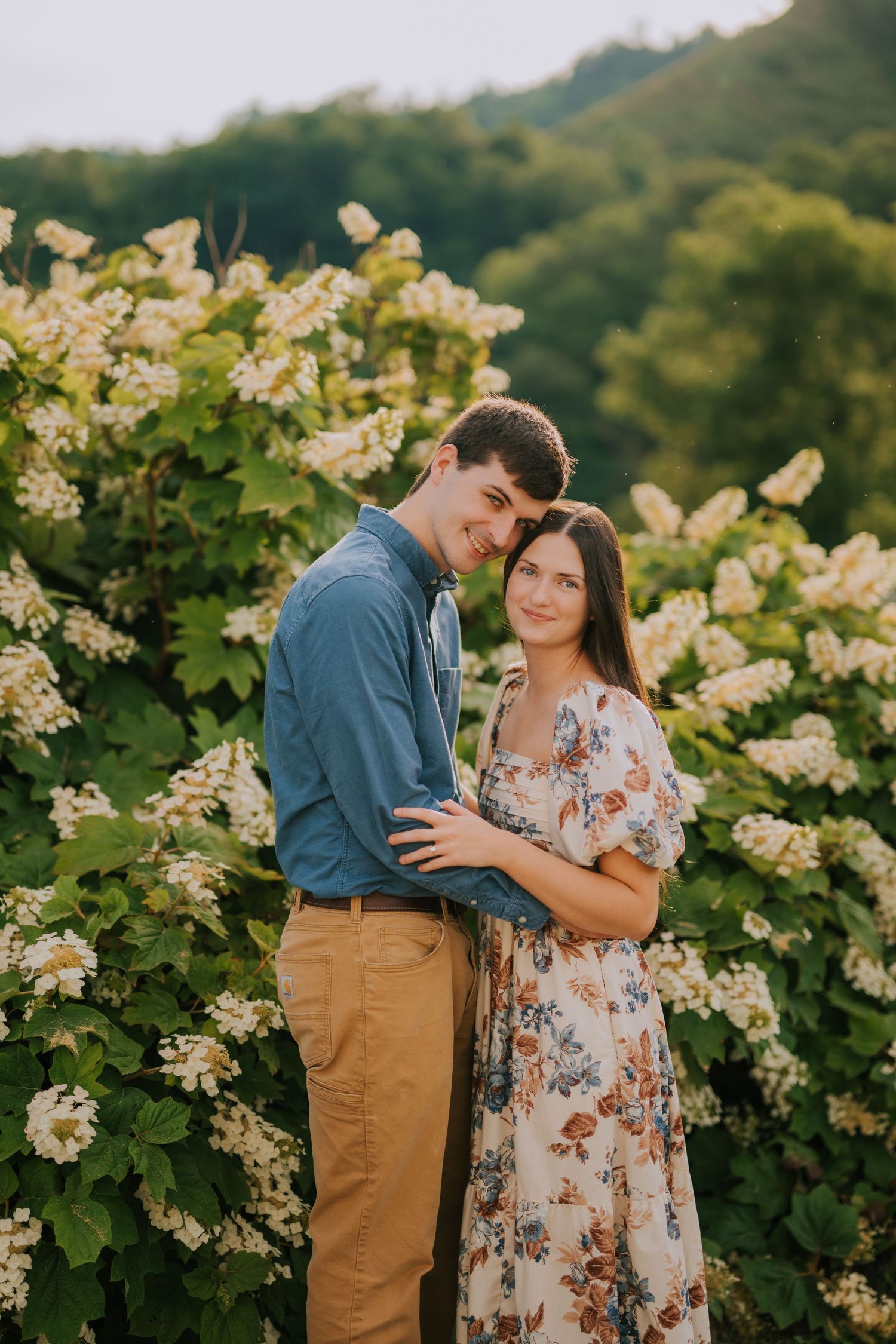 A couple shares intimate moments among blooming white flowers during golden hour.