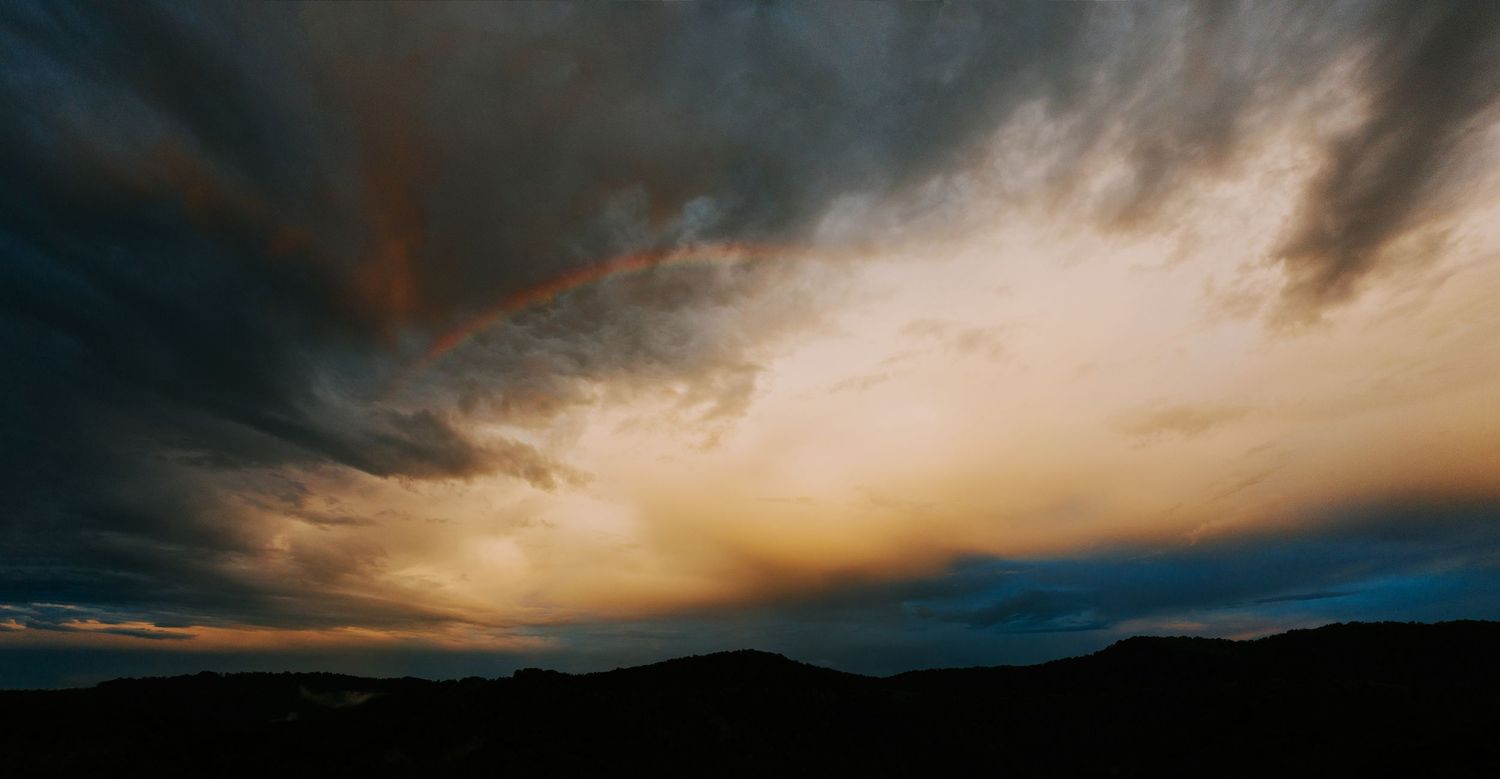 Dramatic sunset sky with dark clouds and golden light over silhouetted mountains.