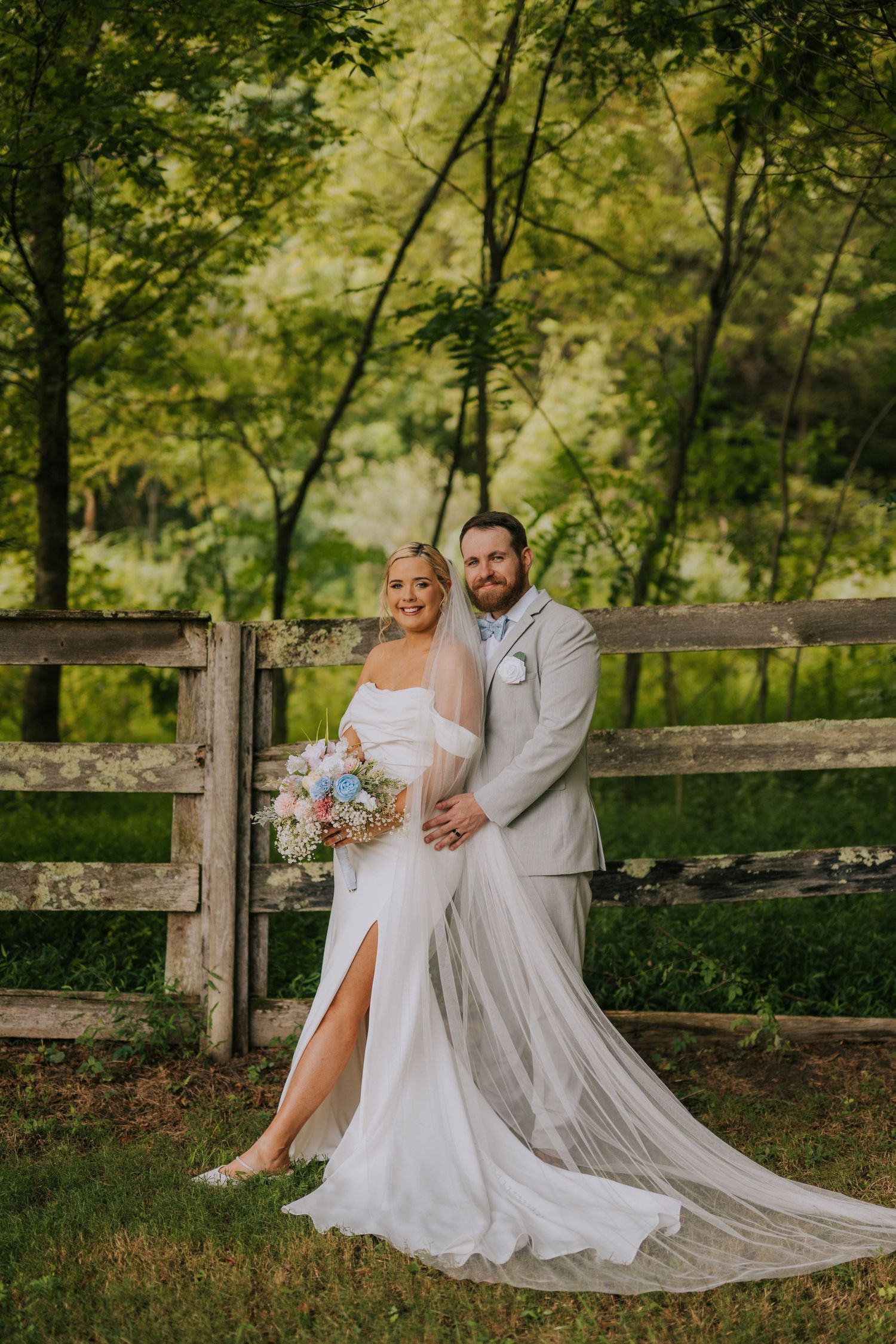 Rustic wedding portraits by wooden fence with bride in flowing white gown.