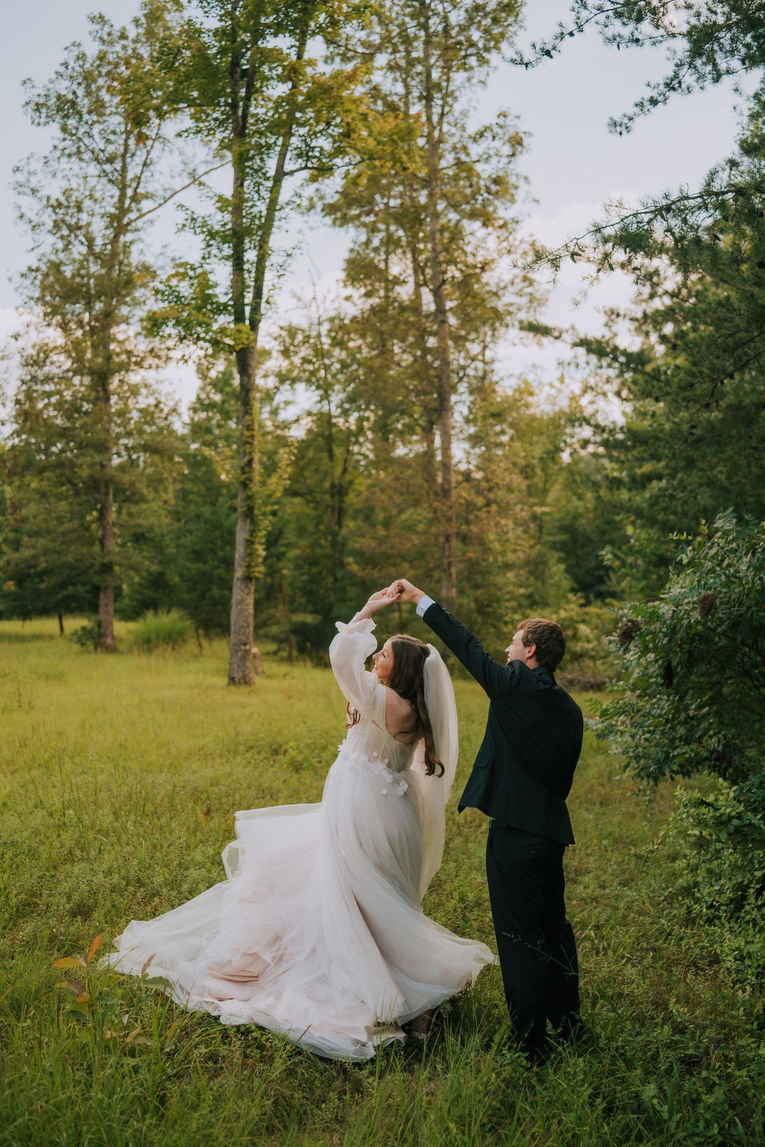 Couple dances and twirls in a sunlit meadow during their wedding photoshoot.