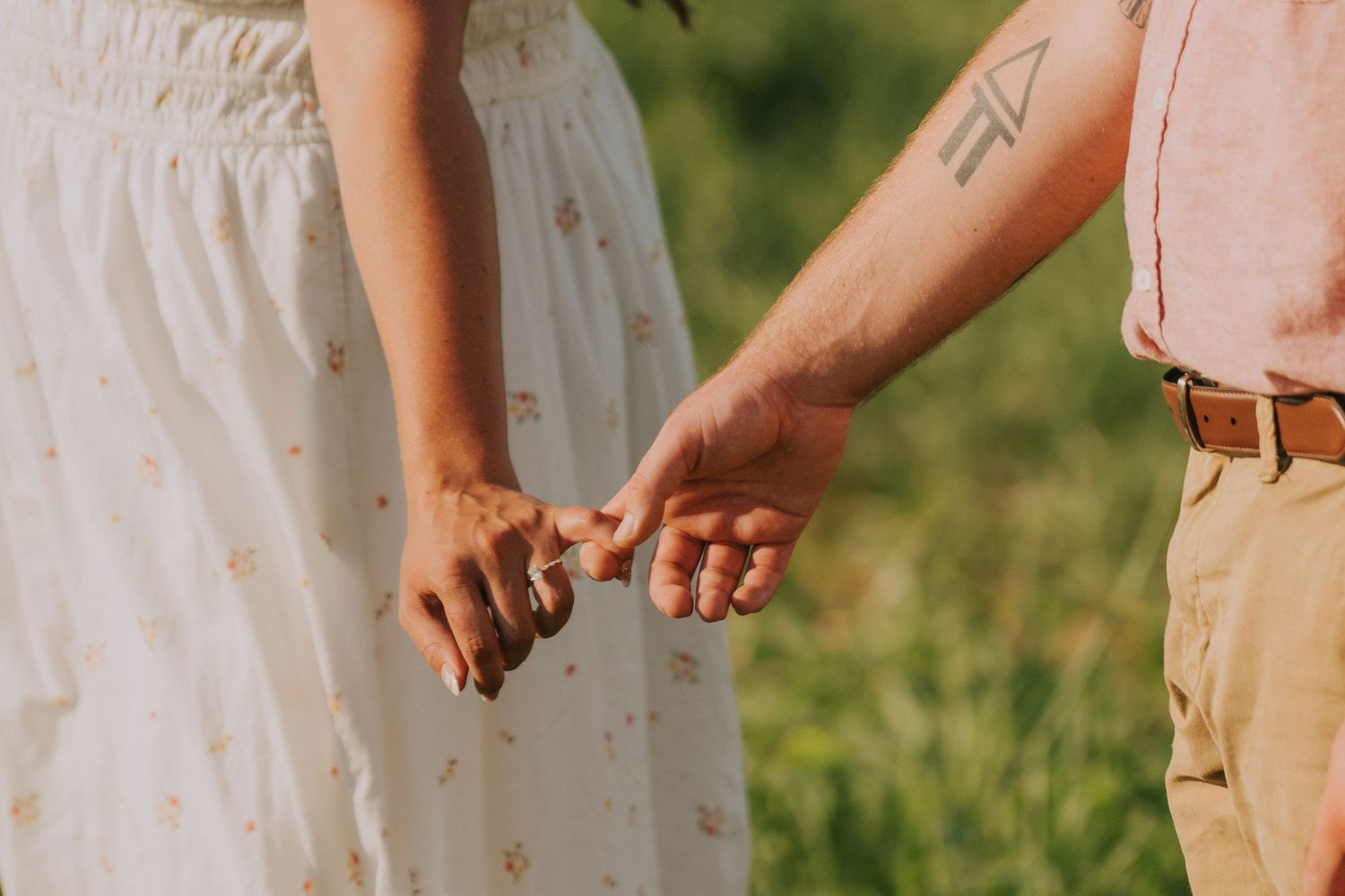 Couple in white dress and pink shirt embrace tenderly in an outdoor setting.