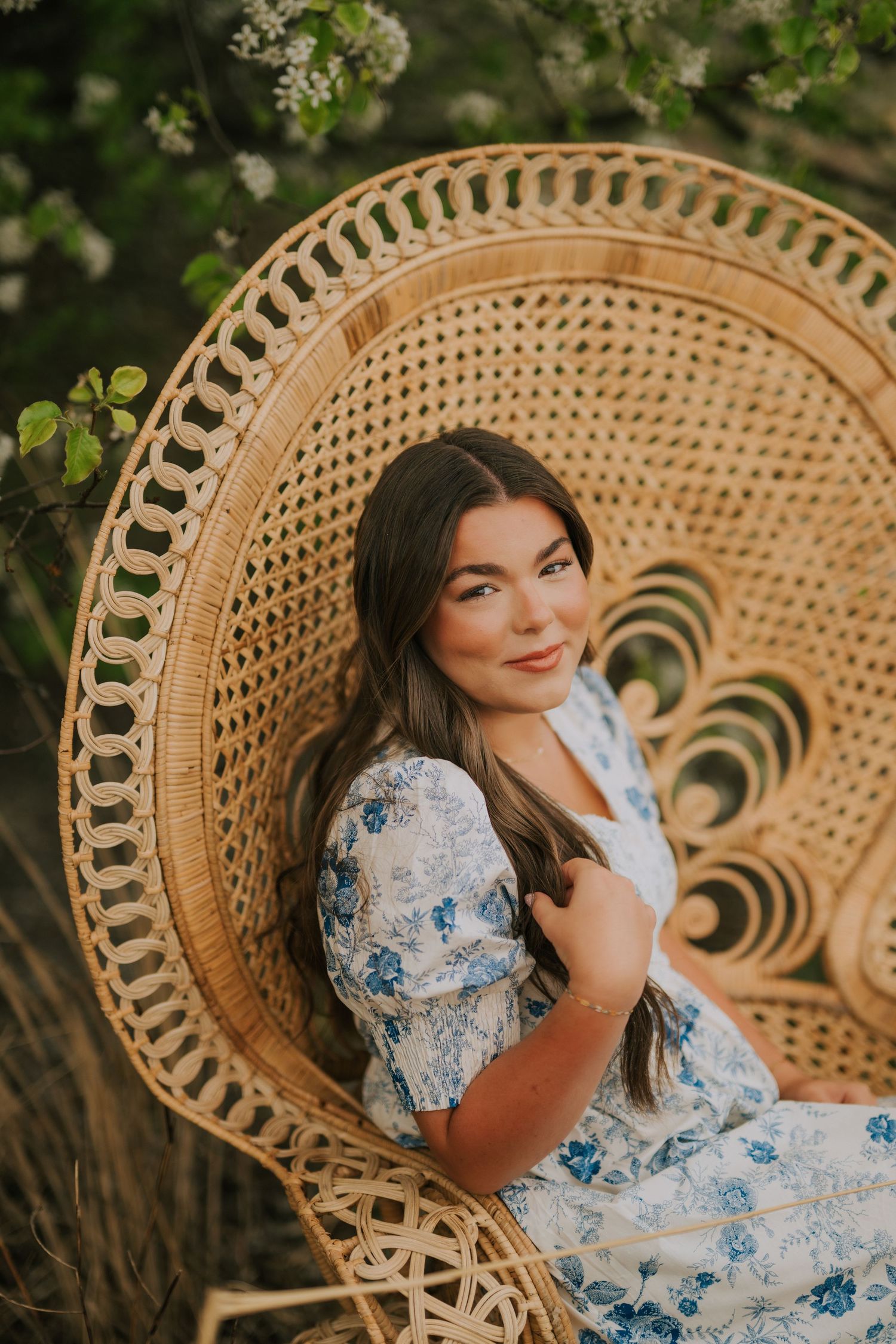Person in blue floral dress seated in ornate peacock wicker chair outdoors.