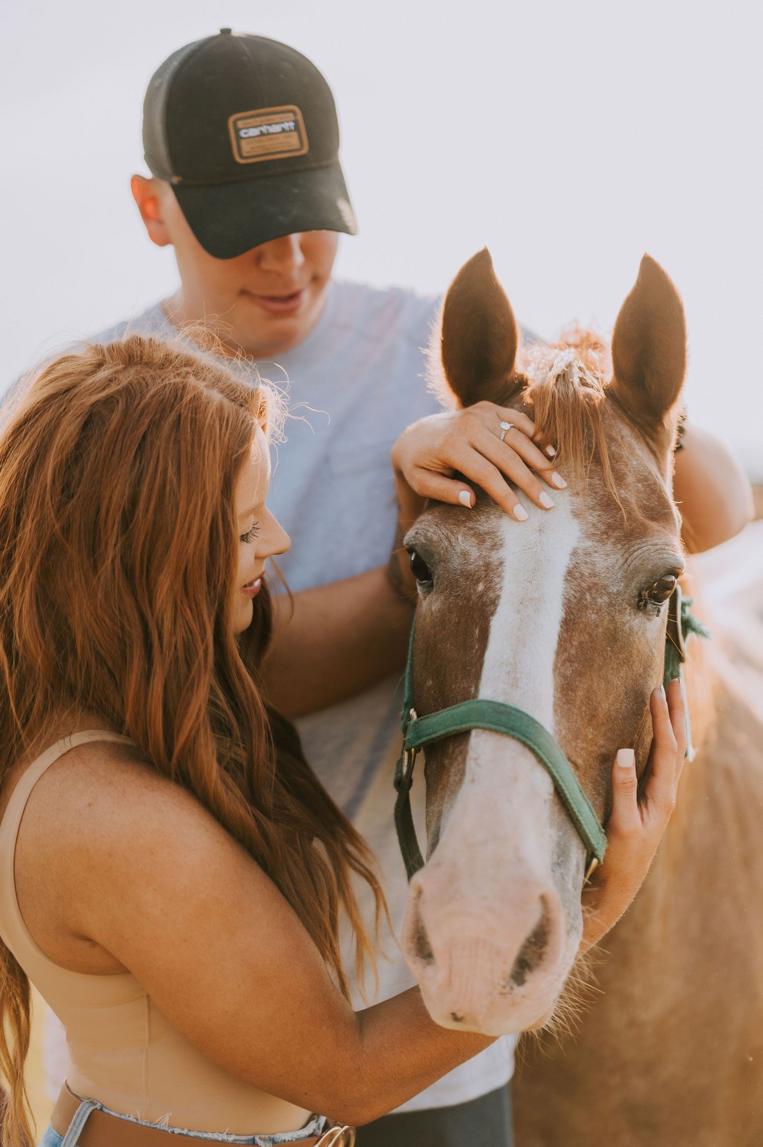 A couple pets and interacts with a horse wearing a green halter.