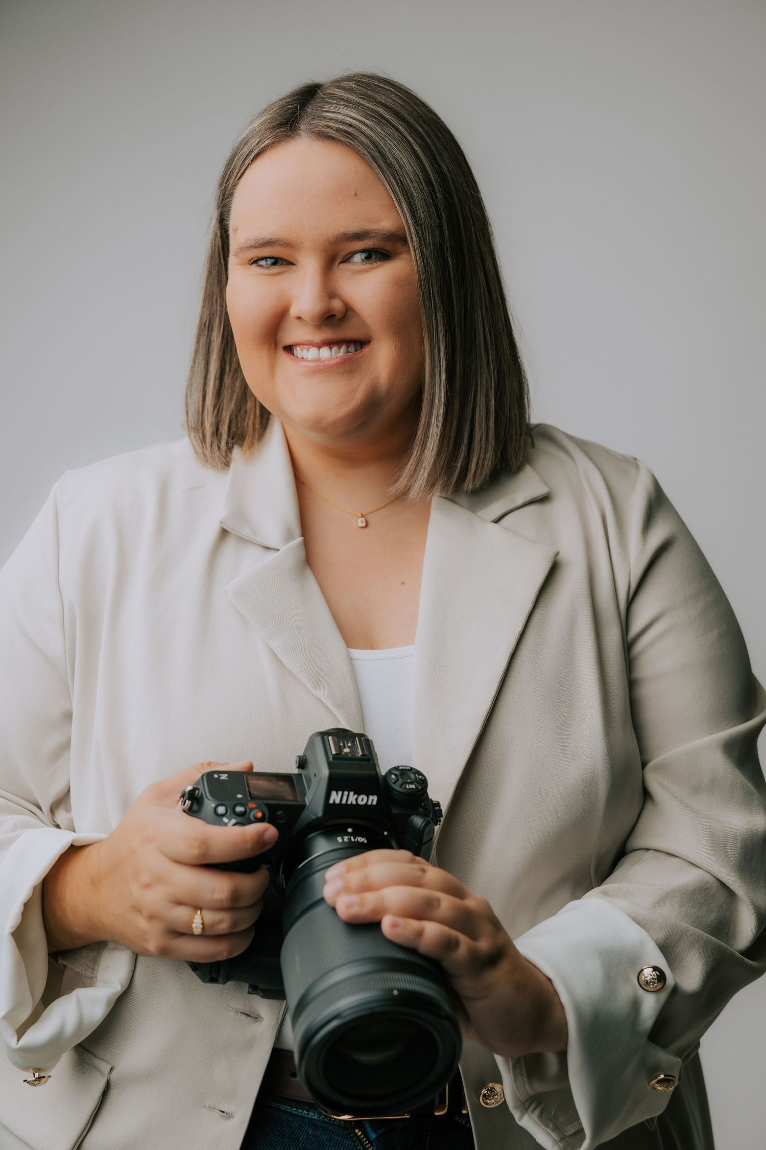 Professional photographer in white blazer demonstrates camera equipment in studio setting.