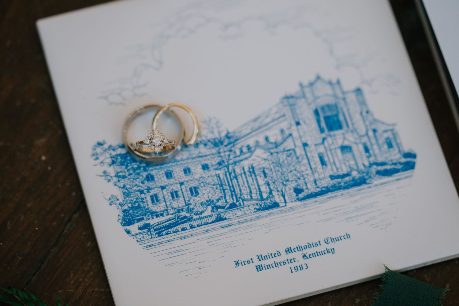 Wedding rings rest on a blue illustration of a church building on what appears to be a wedding invitation or program.