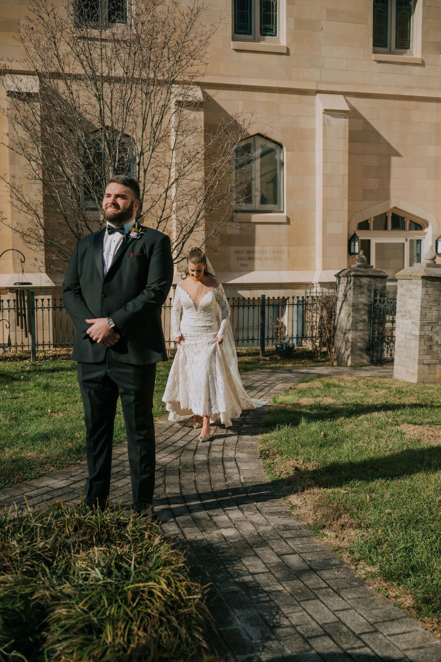 A couple stands outside a stone building during a wedding first look moment on a sunny spring day.