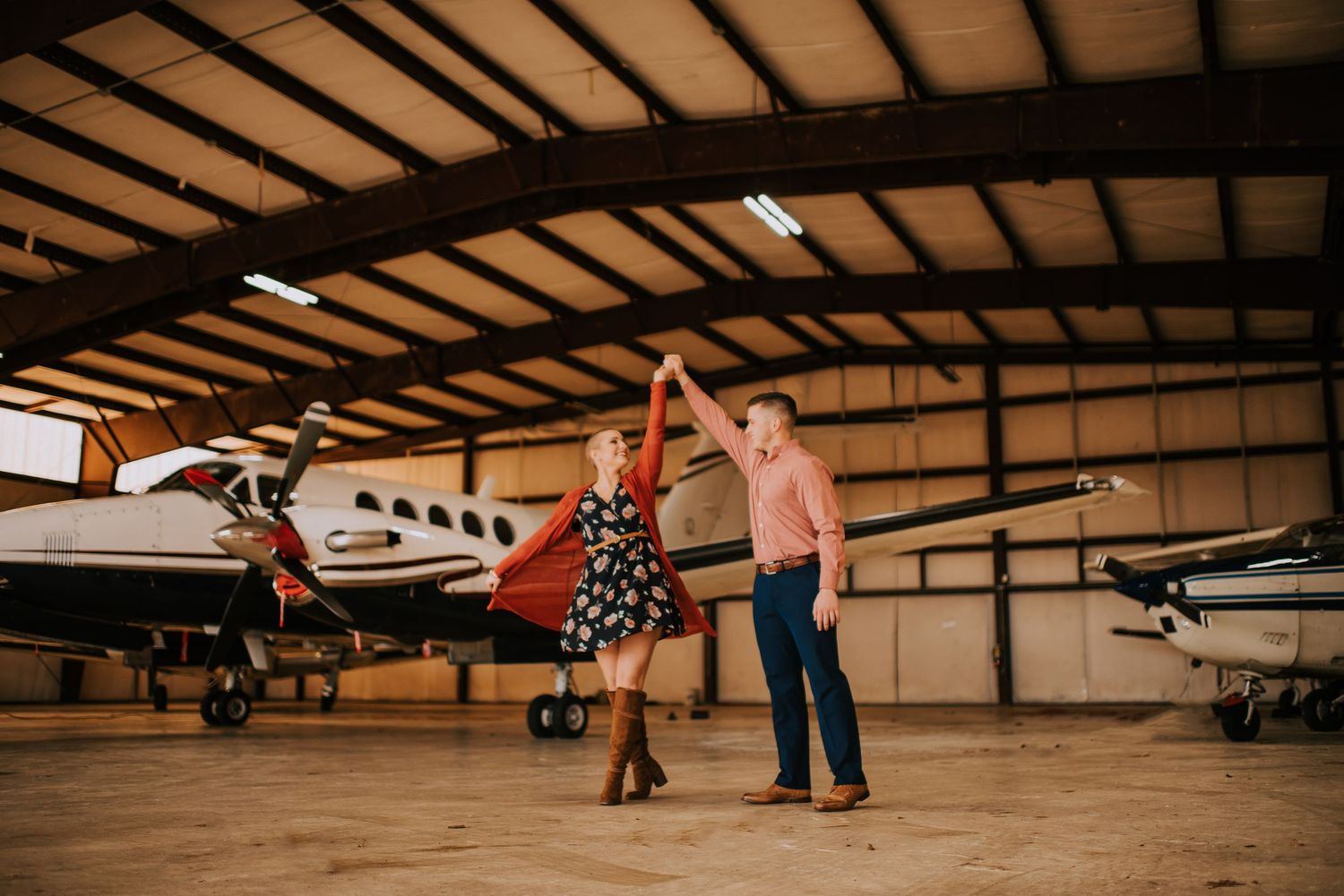 Wide angle view inside an aircraft hangar showing small planes and people.
