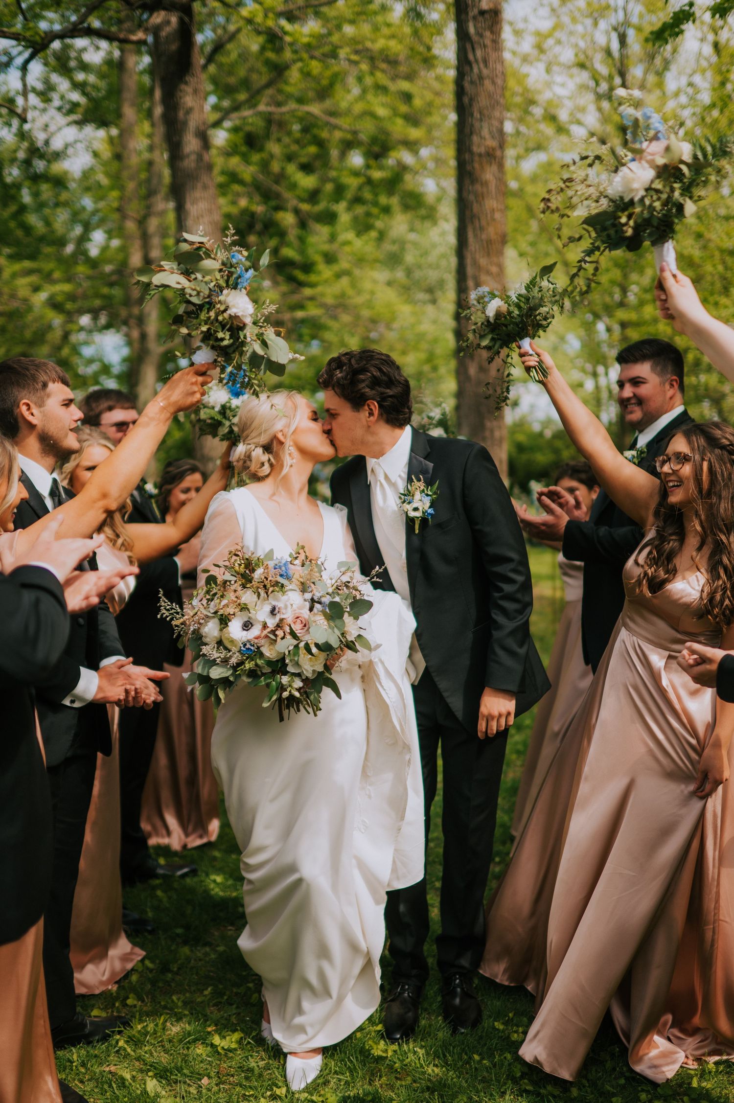 Wedding party celebrating outdoors with joyful poses among trees.