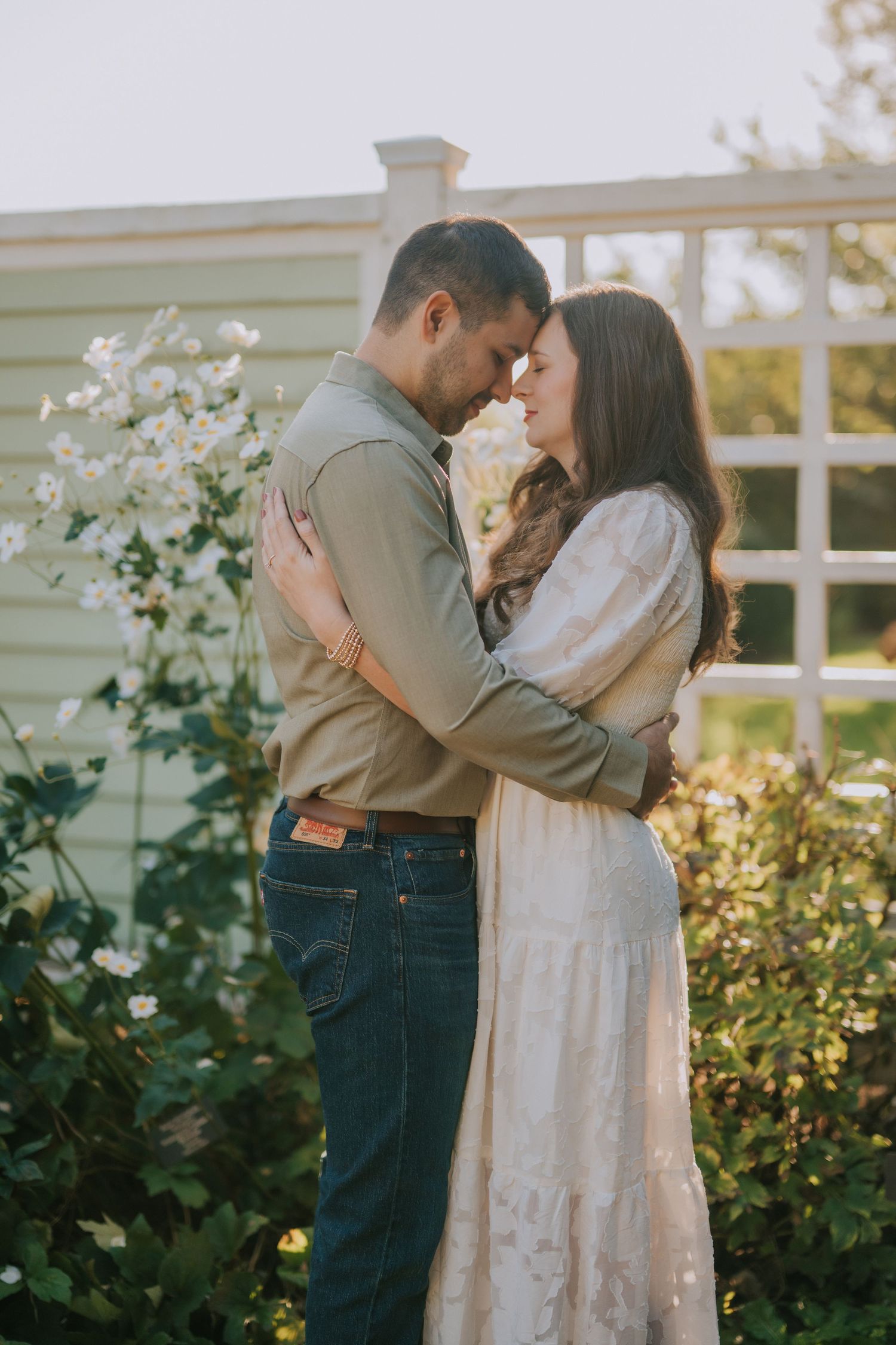 Intimate couple portrait session in a garden with blooming white flowers and warm evening light.