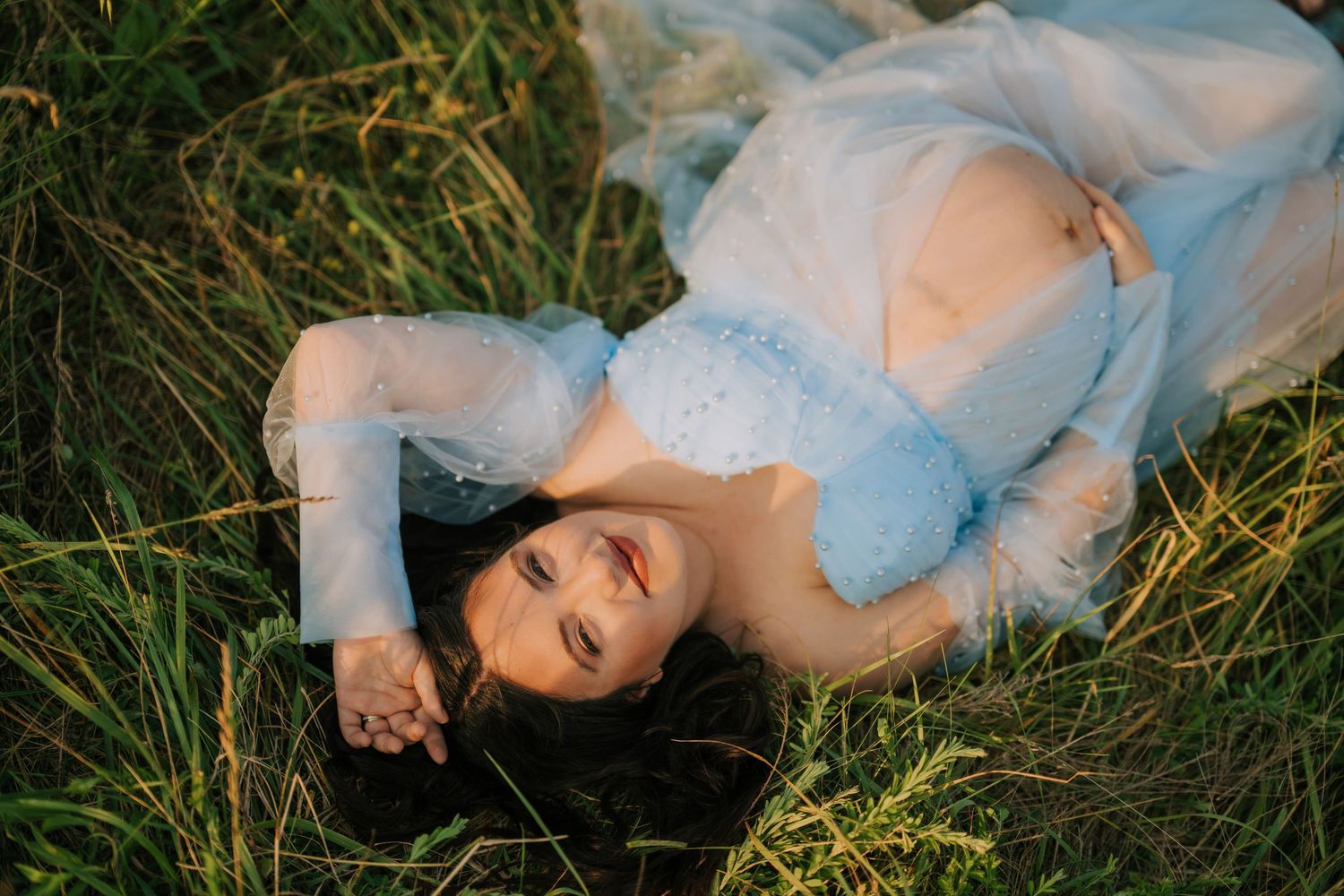 Person in white dress lying in tall grass during golden hour photoshoot.