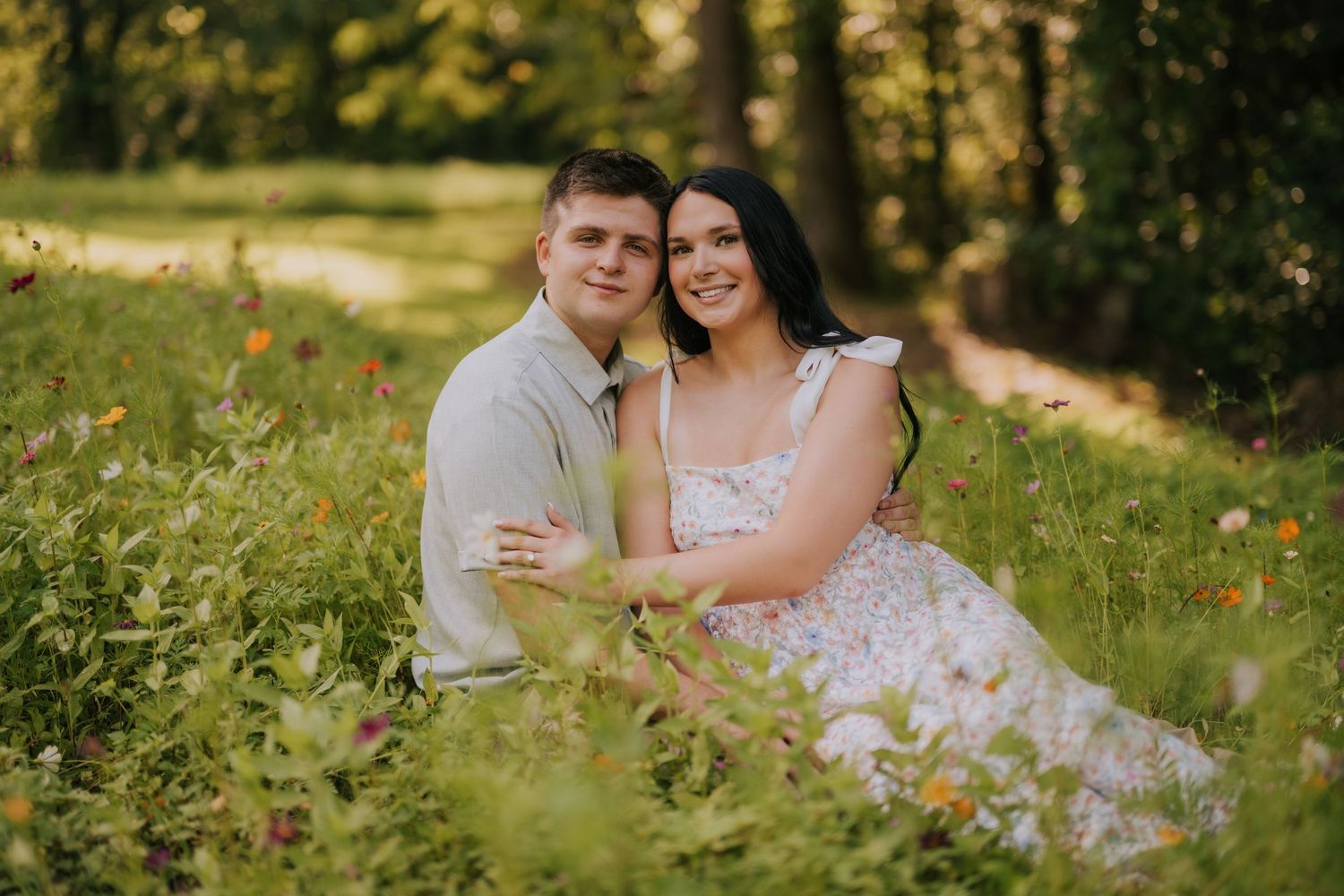 A couple shares an intimate moment in a field with soft natural lighting and green foliage.