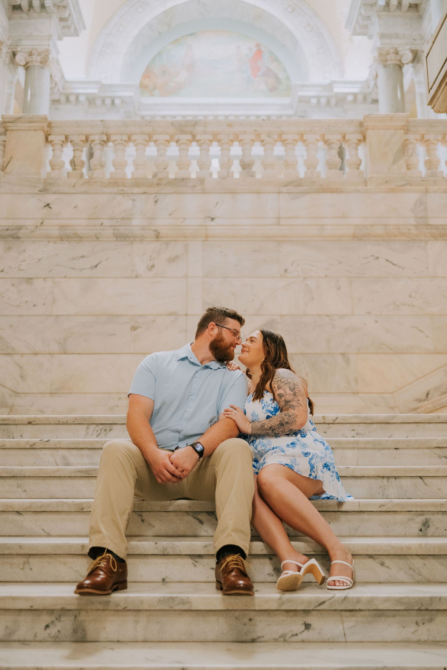 Couple sharing an intimate moment on marble steps in a grand historic building interior.
