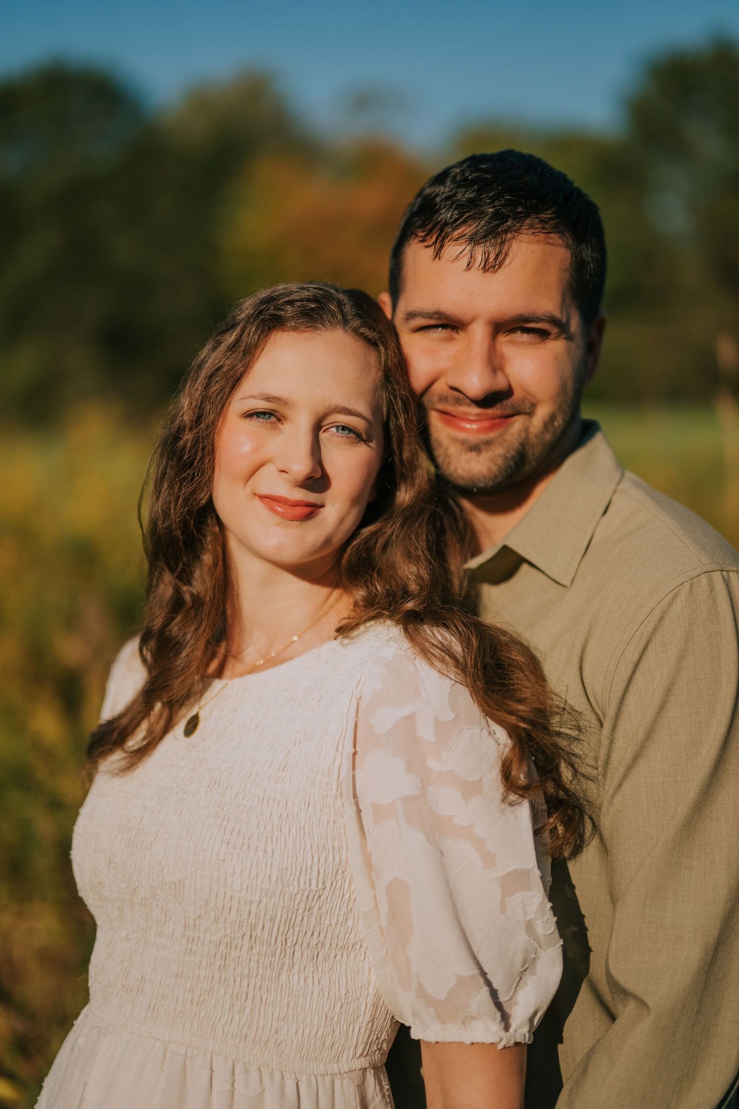 Romantic autumn engagement photoshoot in a field with golden sunlight and natural scenery.