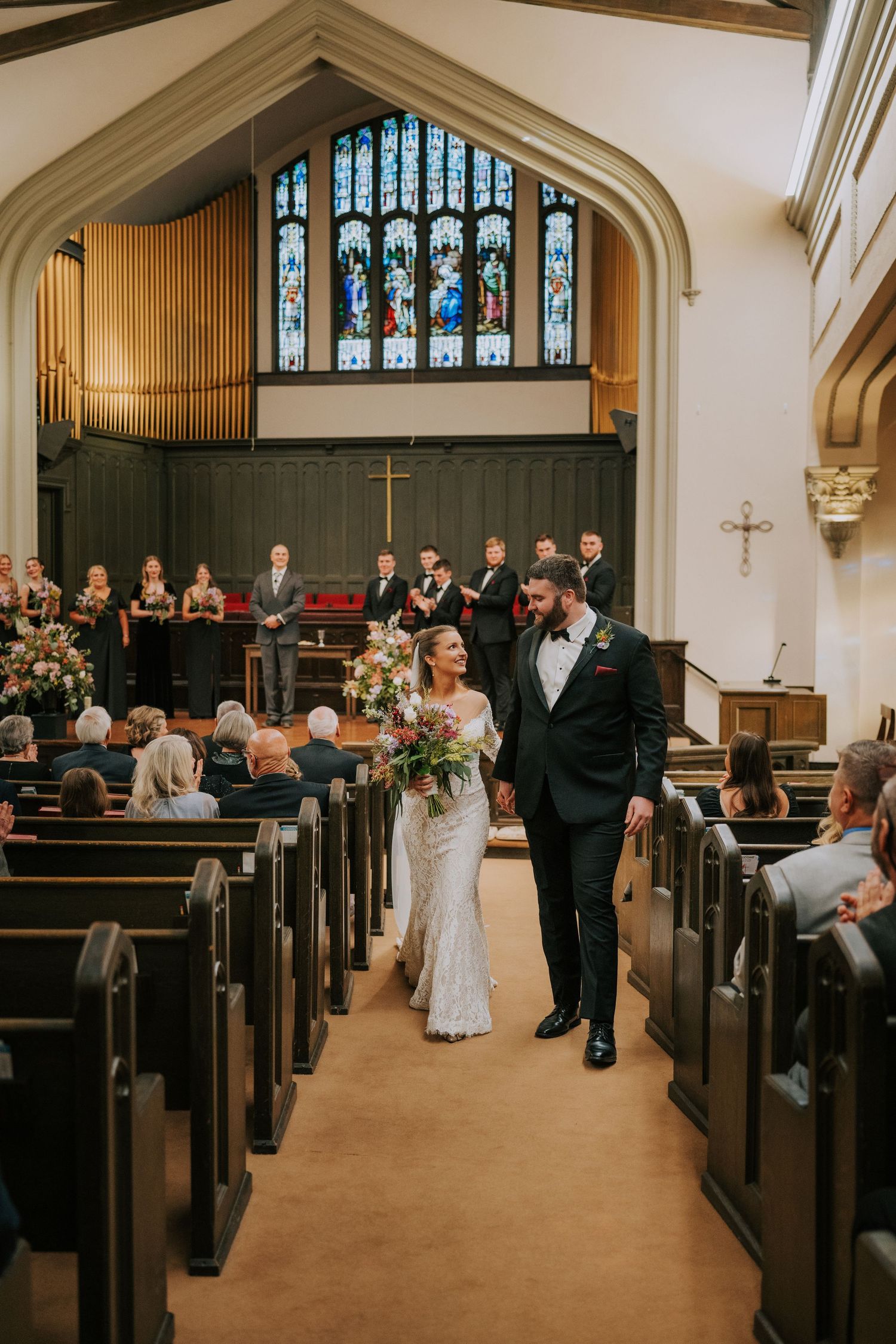 Traditional church wedding ceremony with guests seated in wooden pews and decorative stained glass windows.
