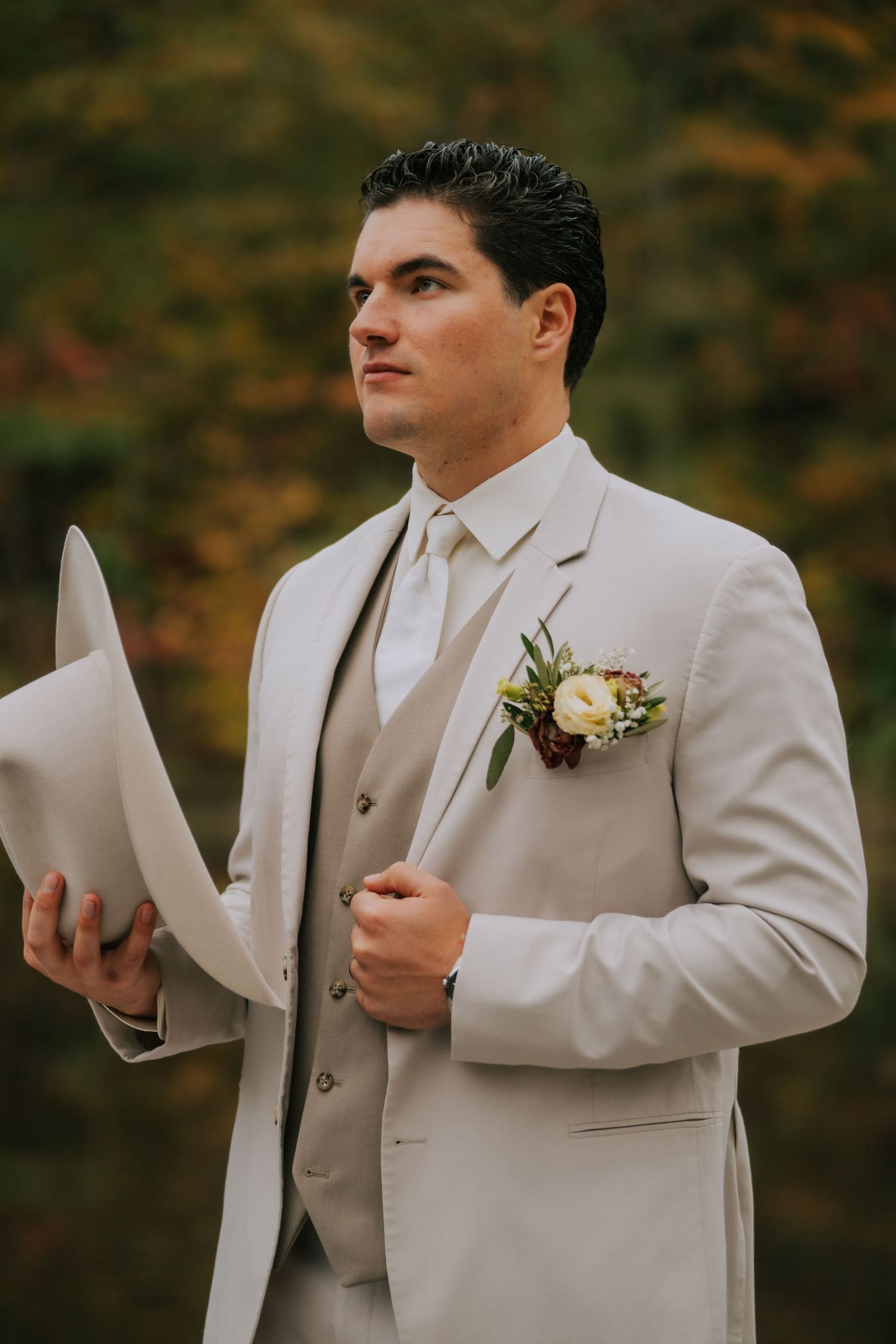 Groom in light beige suit reads from paper during outdoor fall ceremony.