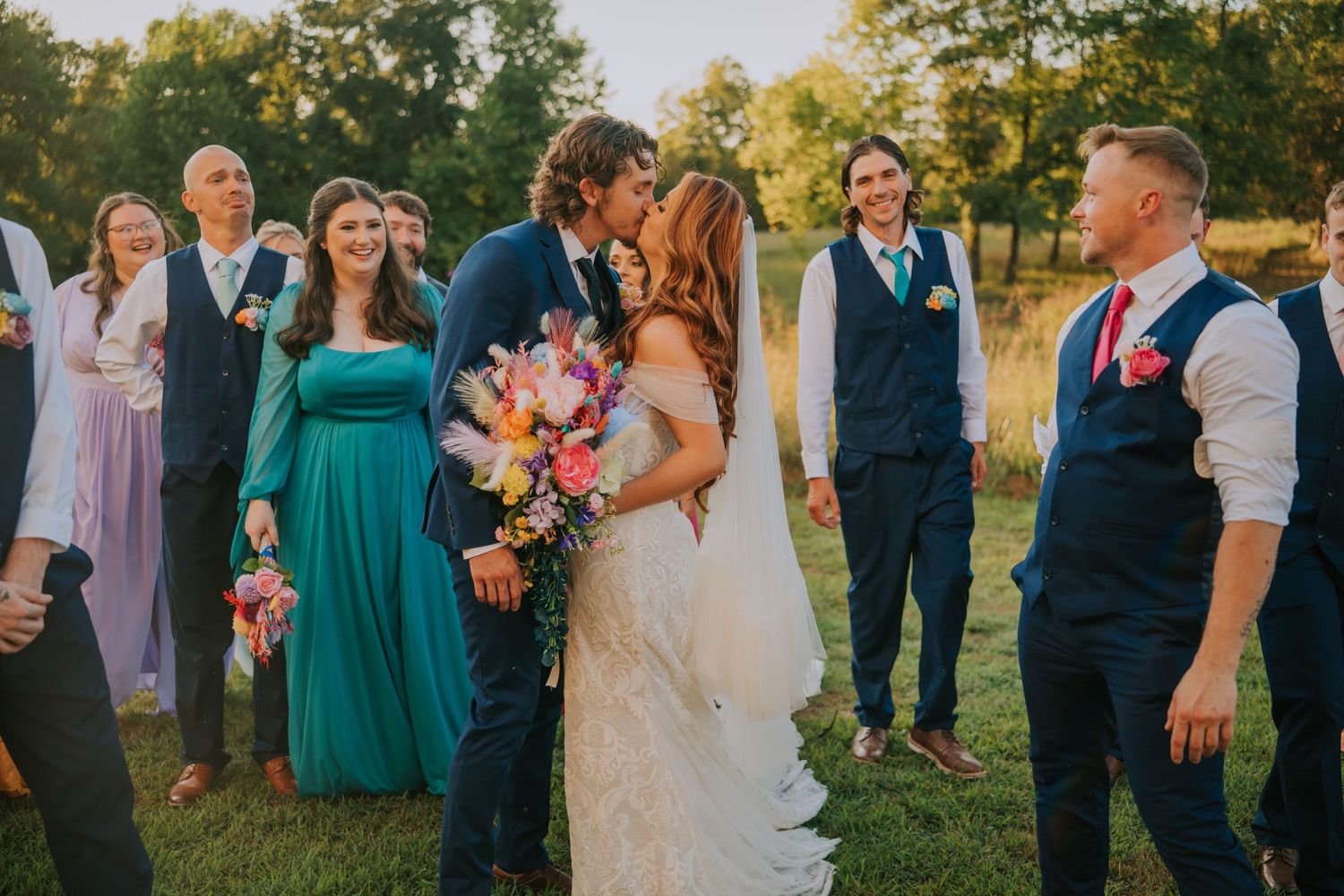 Wedding party in teal and navy attire poses together during golden hour sunset.