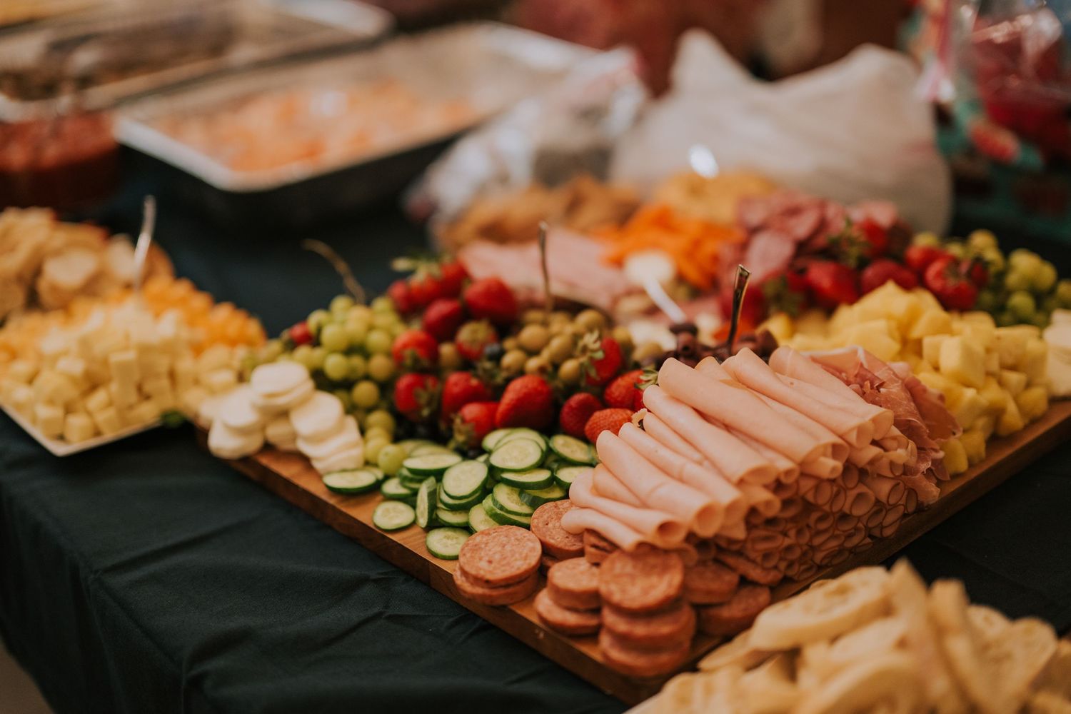 An elegant party platter with sliced meats, cheeses, vegetables, and appetizers displayed on a dark tablecloth.