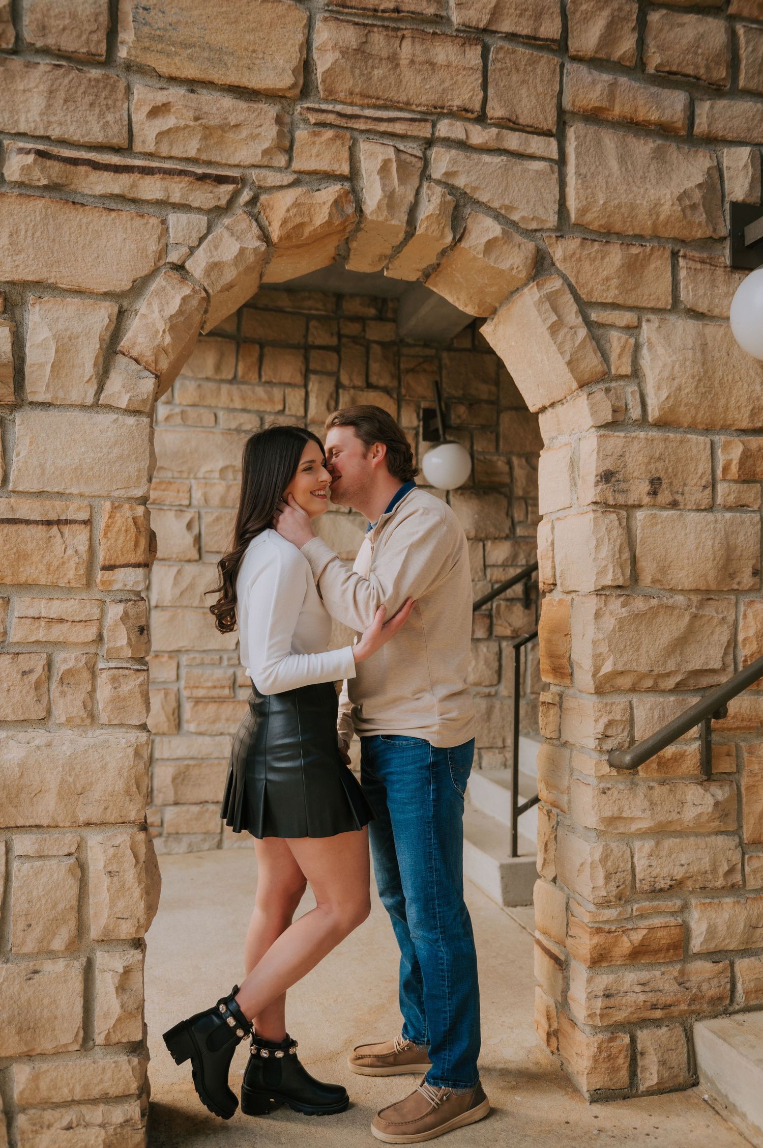 Intimate couple poses against rustic stone wall archways in an artistic photoshoot.