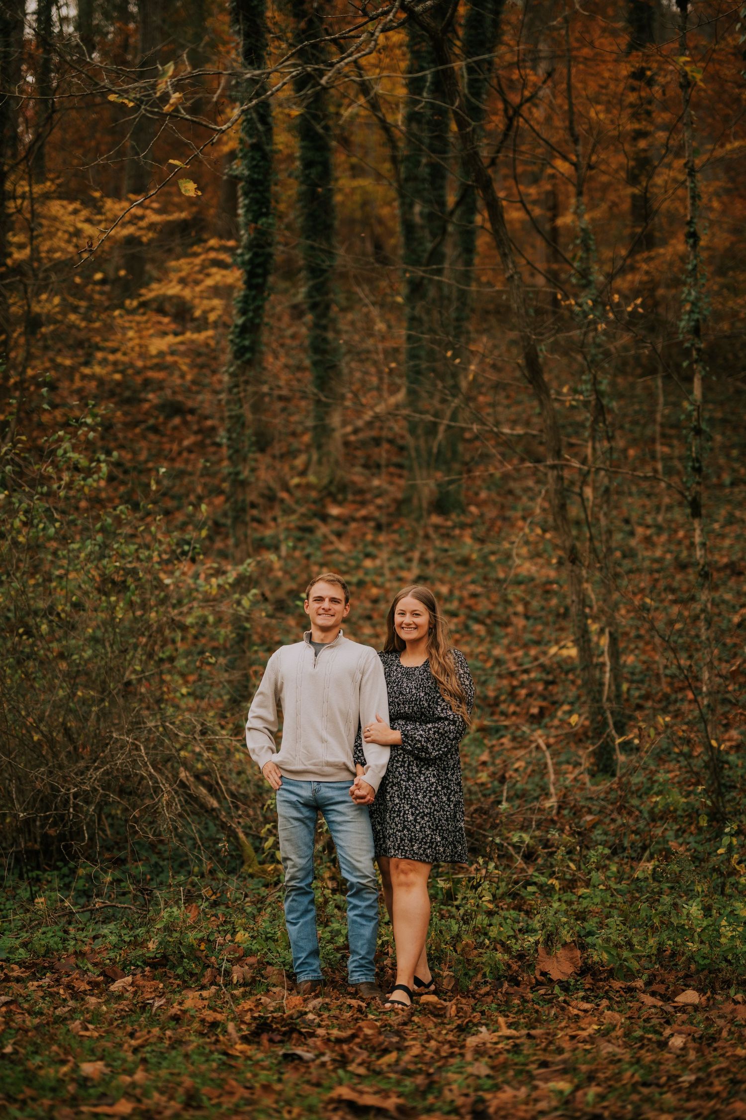 A couple strolls through a forest filled with golden autumn foliage.
