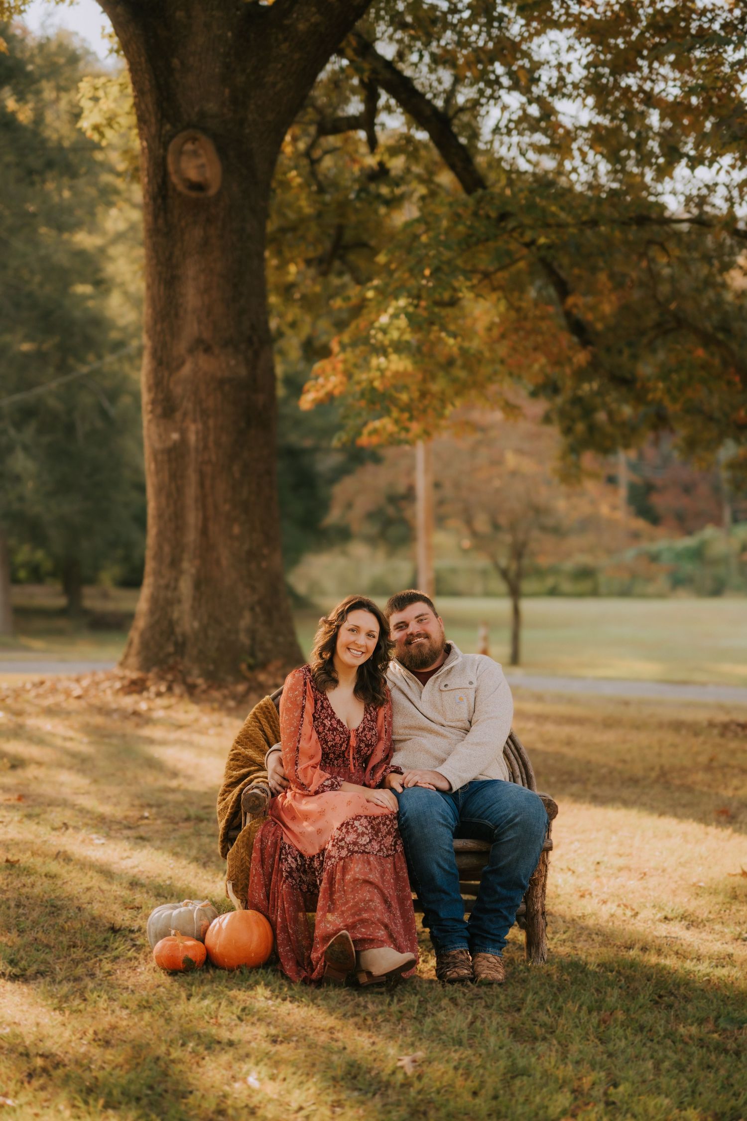 Fall engagement session with pumpkins under golden autumn trees.