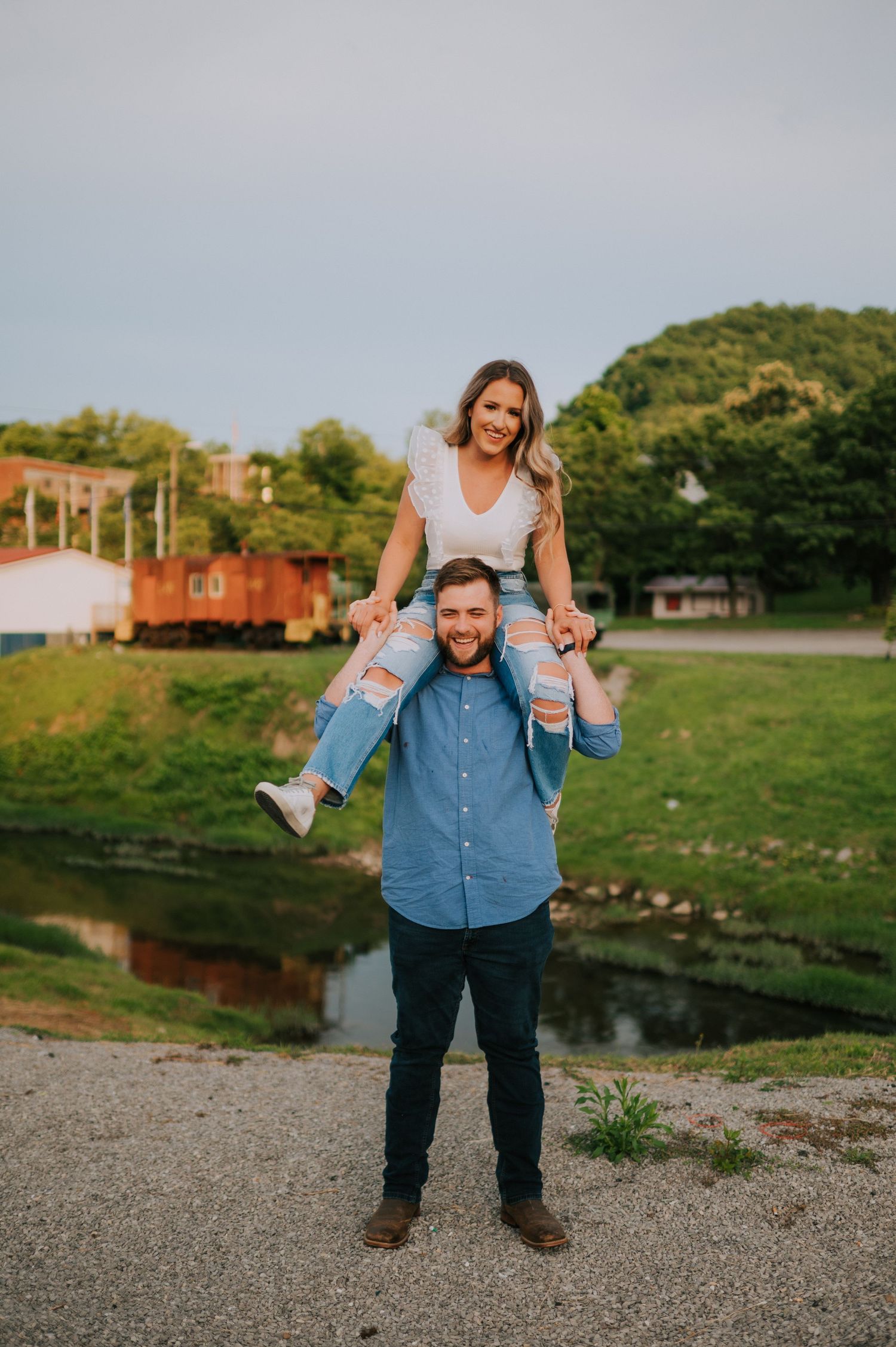 A family shares a playful moment near a waterfront with green hills in the background.