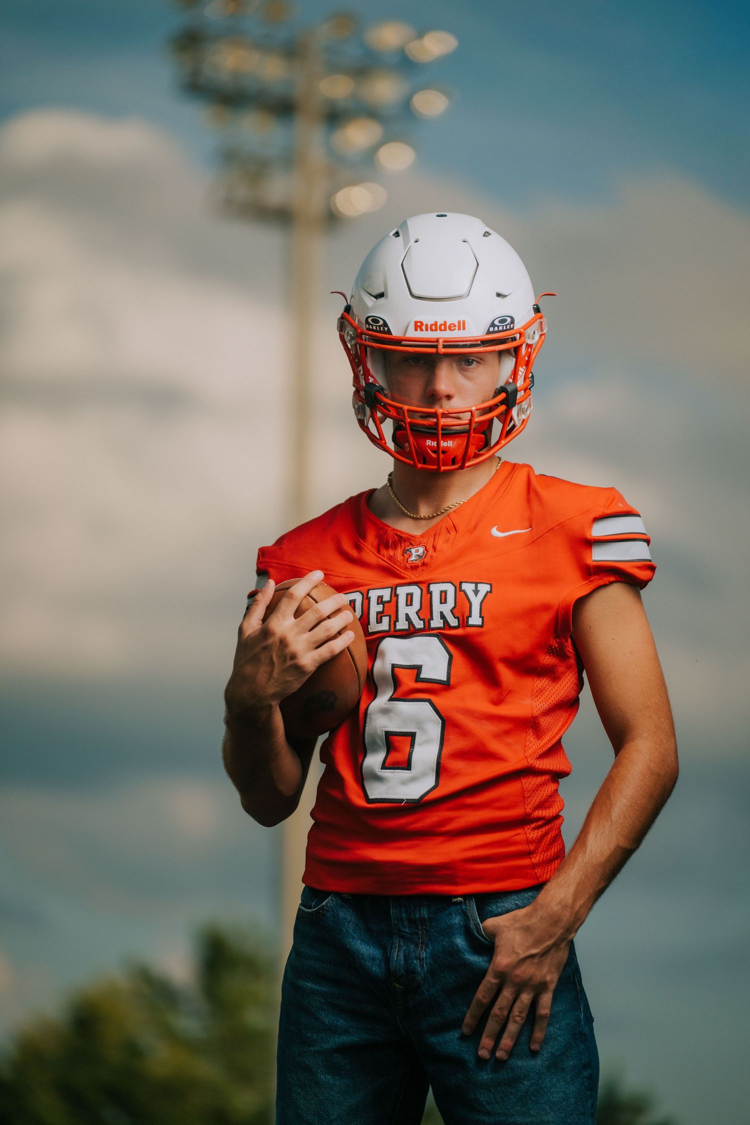 A football player in an orange jersey and white helmet poses against a blue sky.