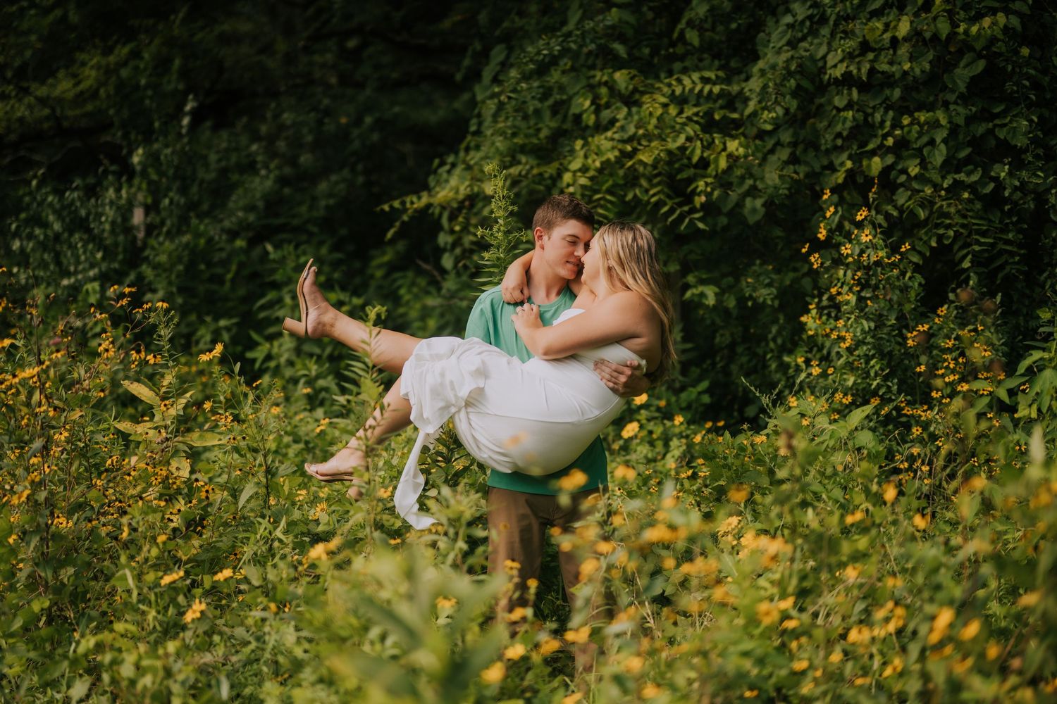 Playful couple posing in field of yellow wildflowers during golden hour.