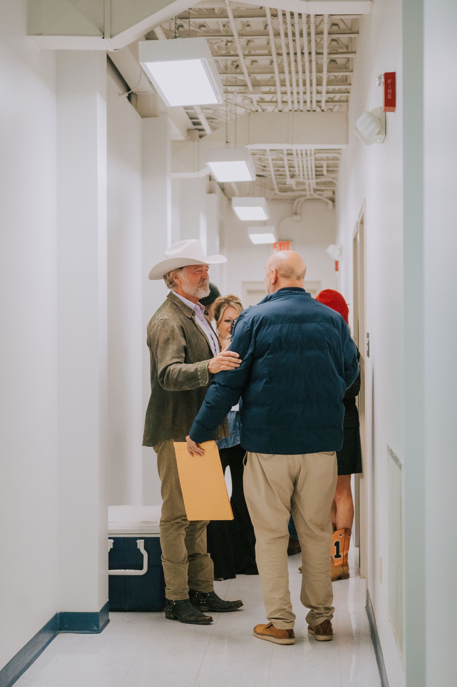People gathered in conversation while standing in a white hallway with fluorescent lights and exposed ceiling.