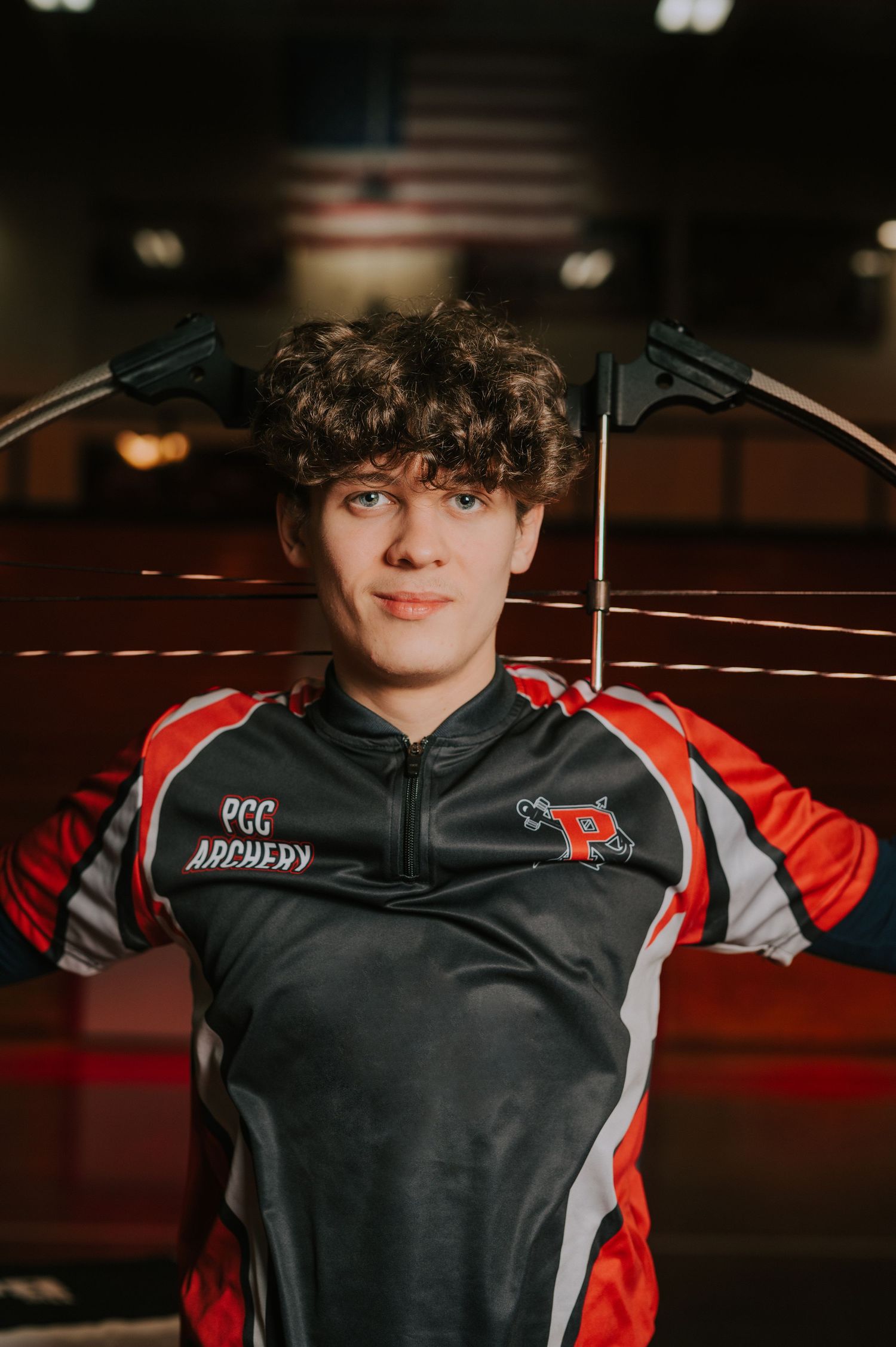 Student athlete in red and black archery uniform poses for sports portrait.