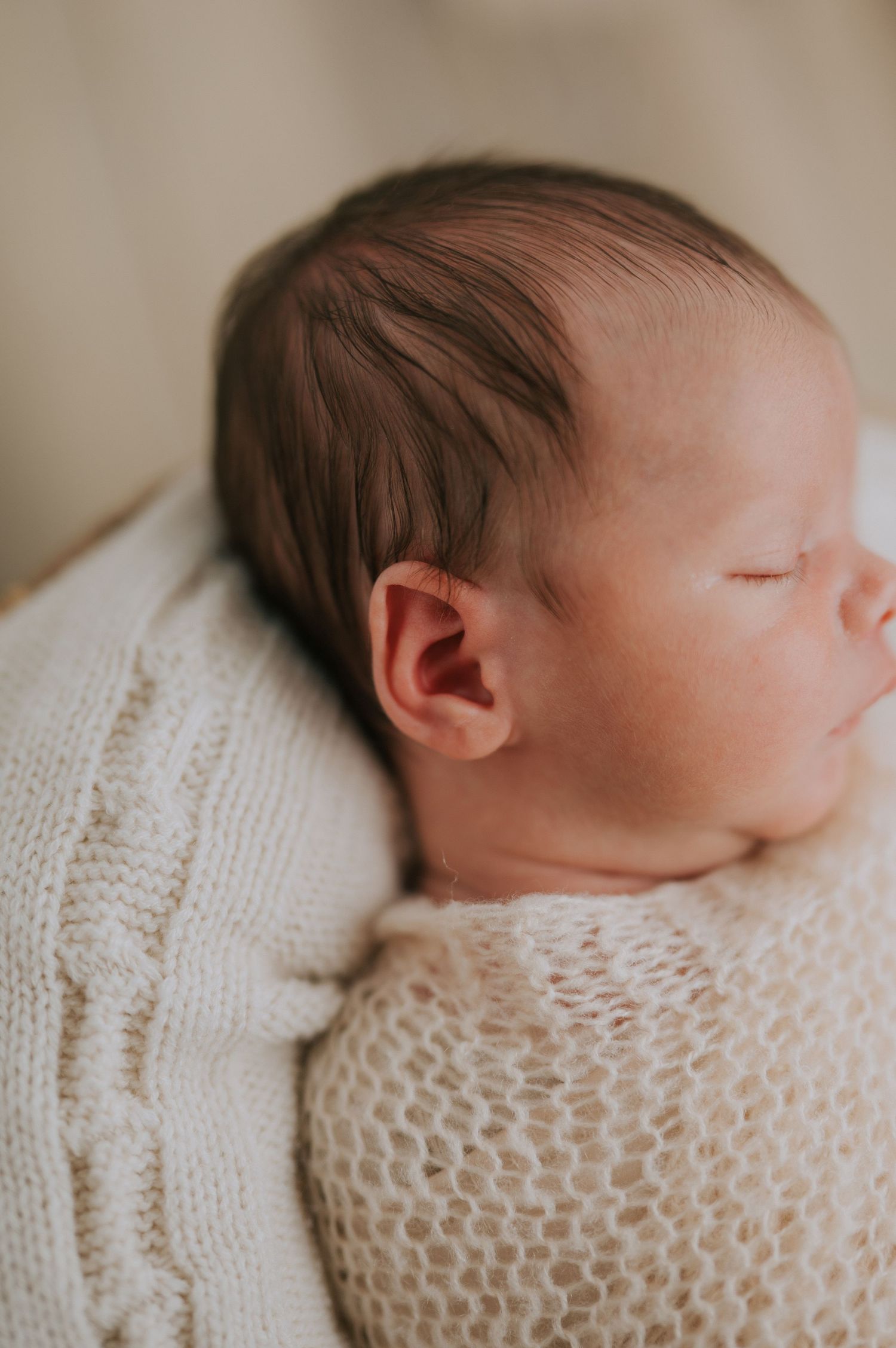 Peaceful sleeping newborn swaddled in soft white knitted wrap.