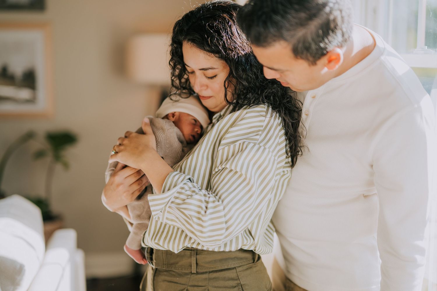 A tender family moment at home as parents embrace their newborn baby in soft natural lighting.