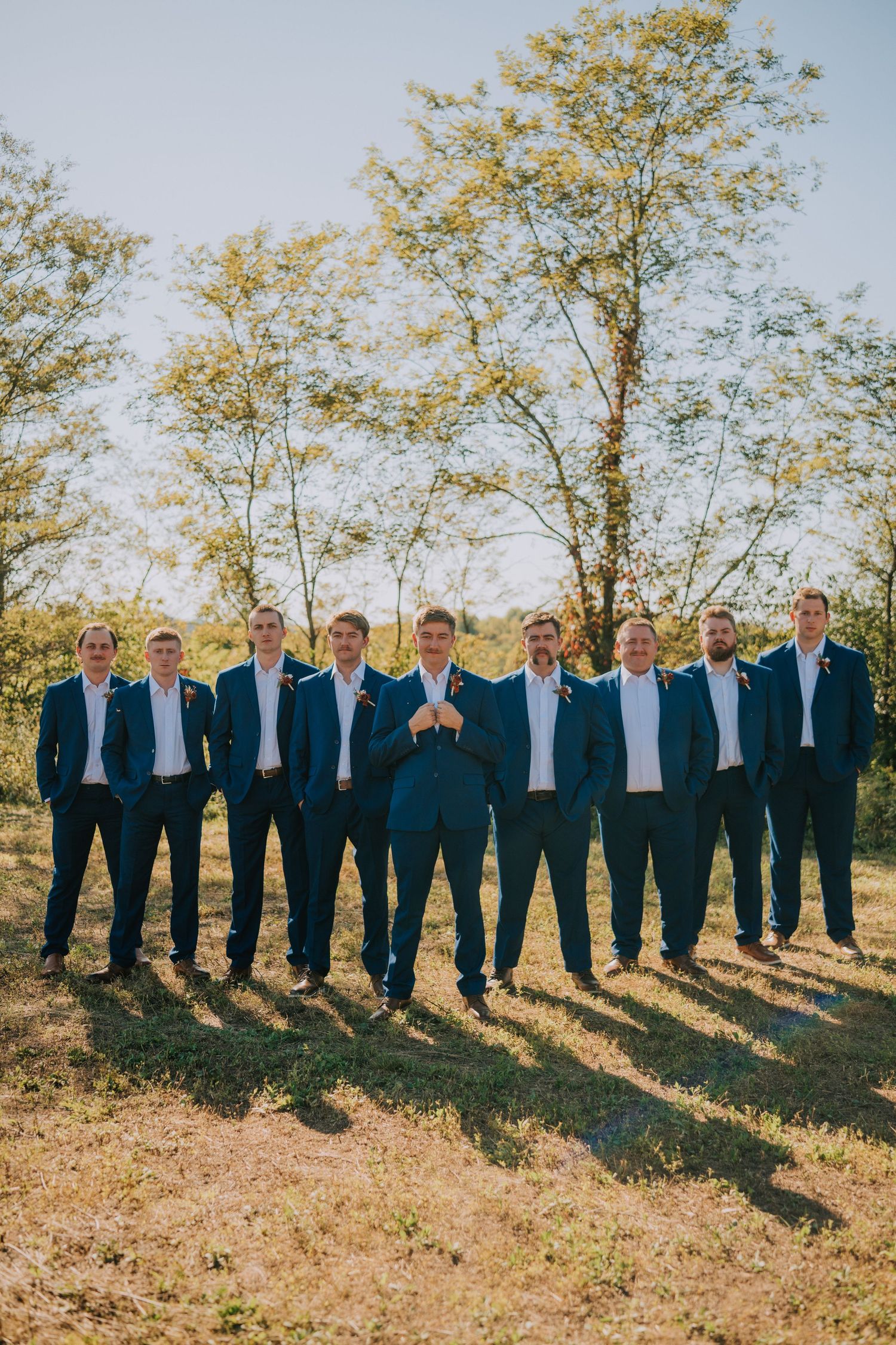 Groomsmen in navy suits lined up on hillside during autumn wedding.