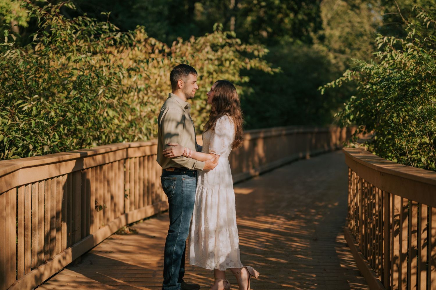 A romantic engagement photo session on a wooden deck surrounded by lush greenery at golden hour.