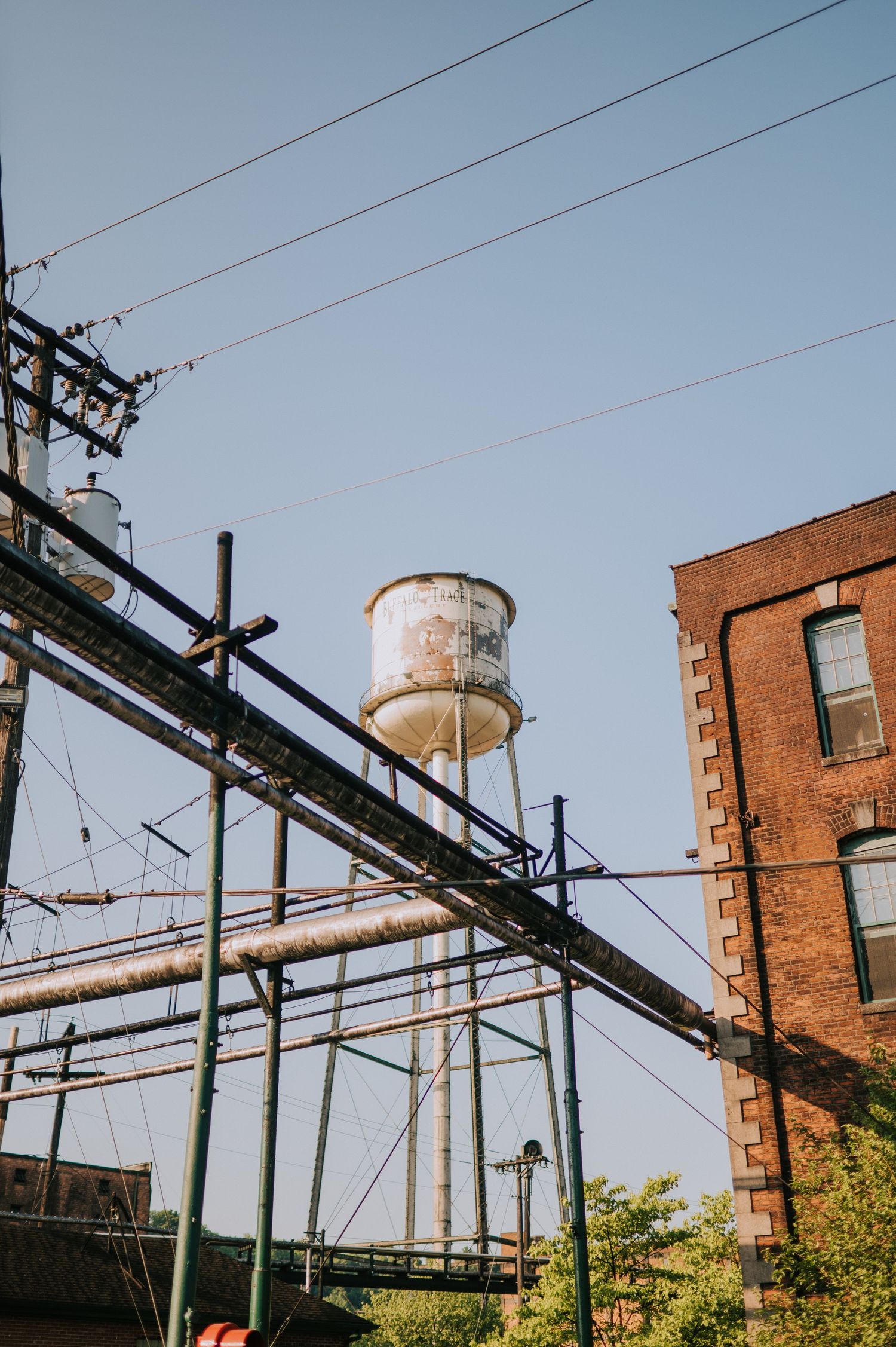 Industrial brick building exterior with water towers and power lines against a blue sky.
