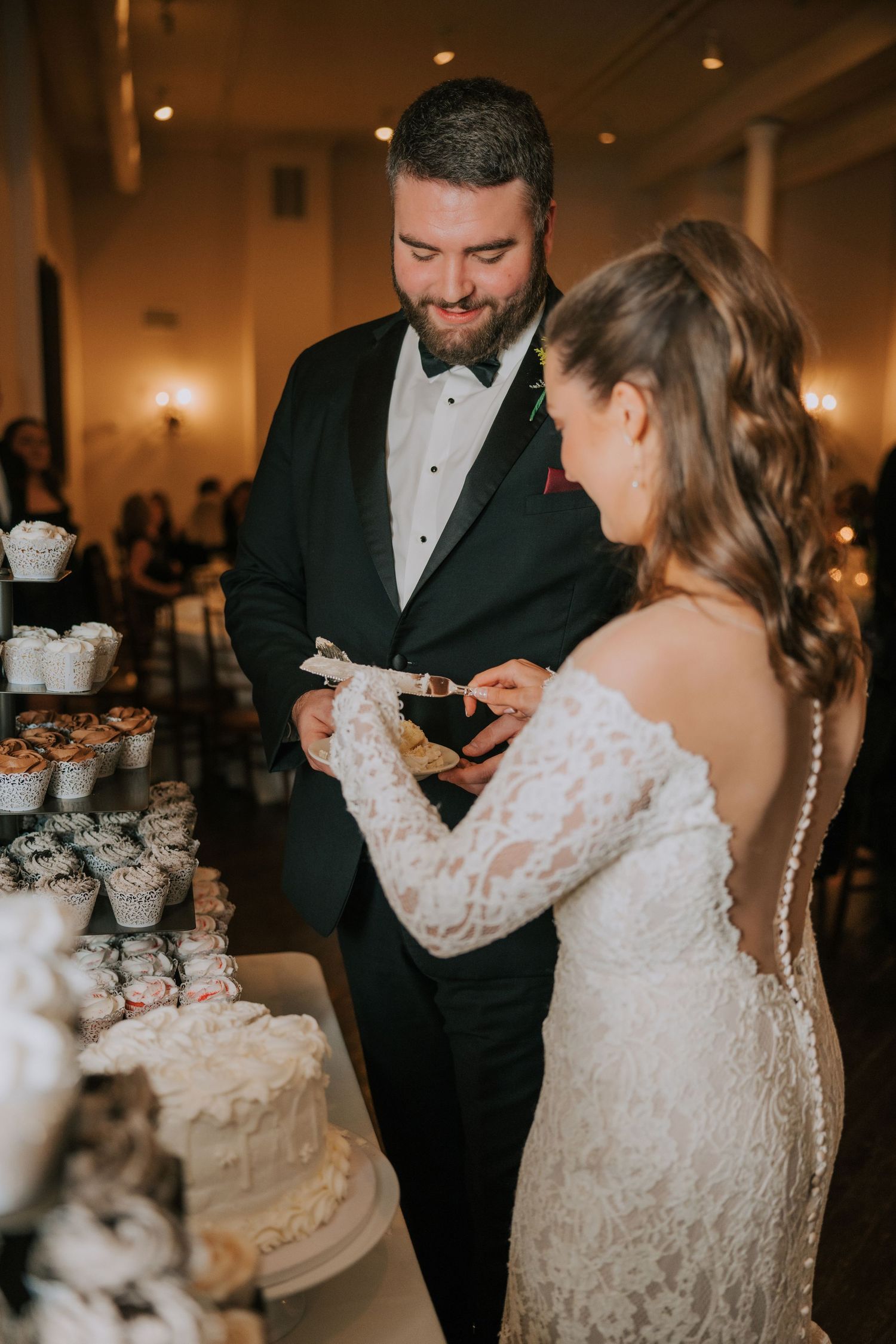 Newlyweds share their first bite of wedding cake together at an elegant reception with cupcake tower display.