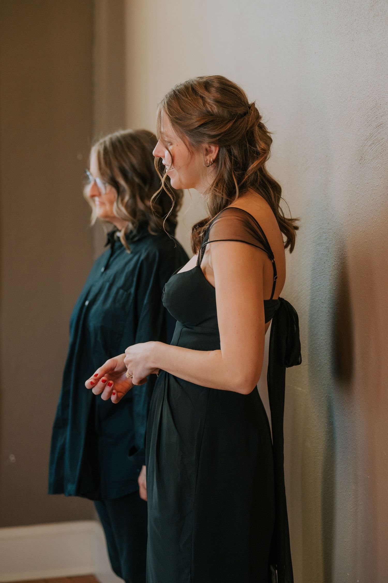 Two people in elegant black dresses stand together during a formal event preparation.