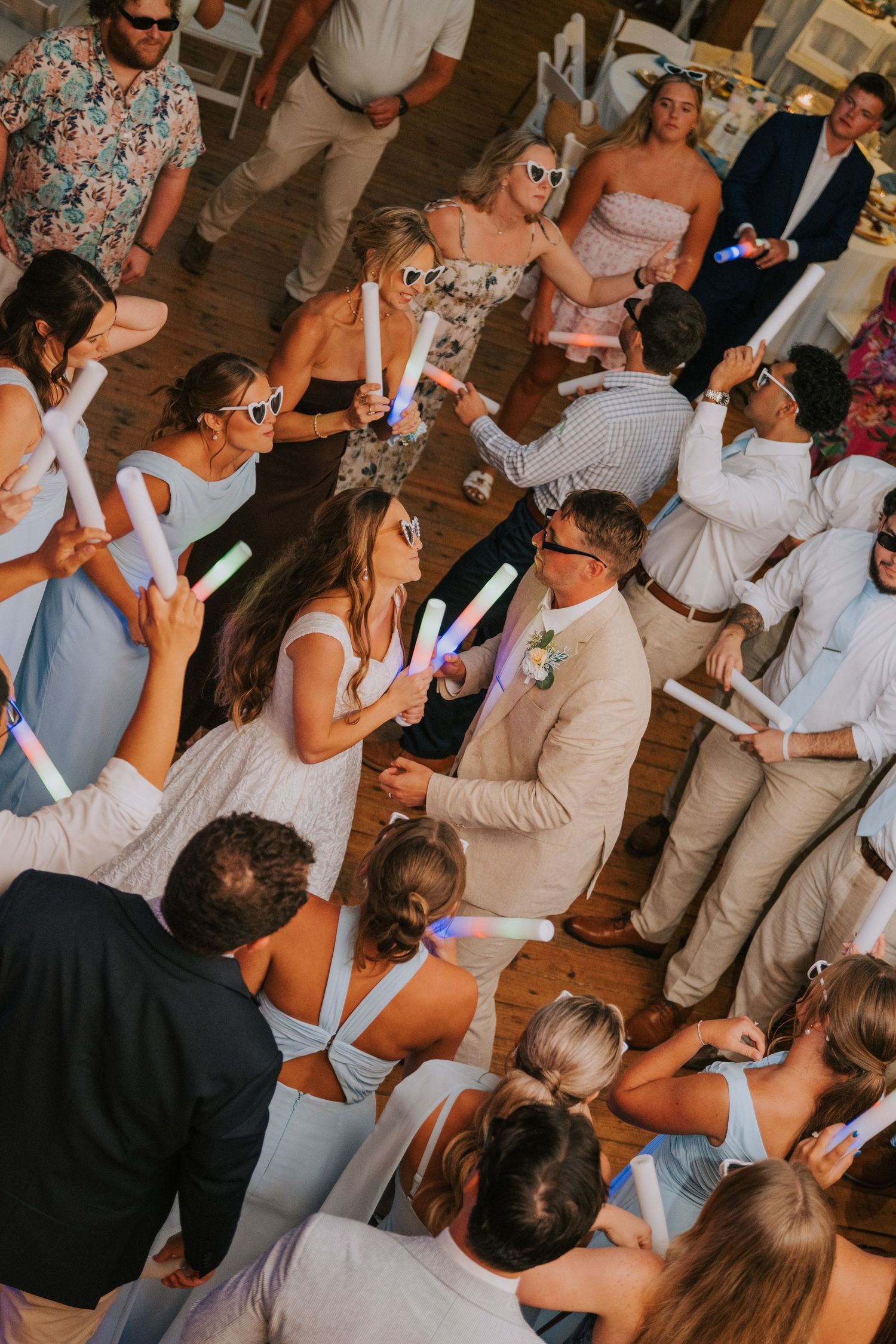 Wedding guests dancing with glowing foam sticks at a lively outdoor reception celebration.