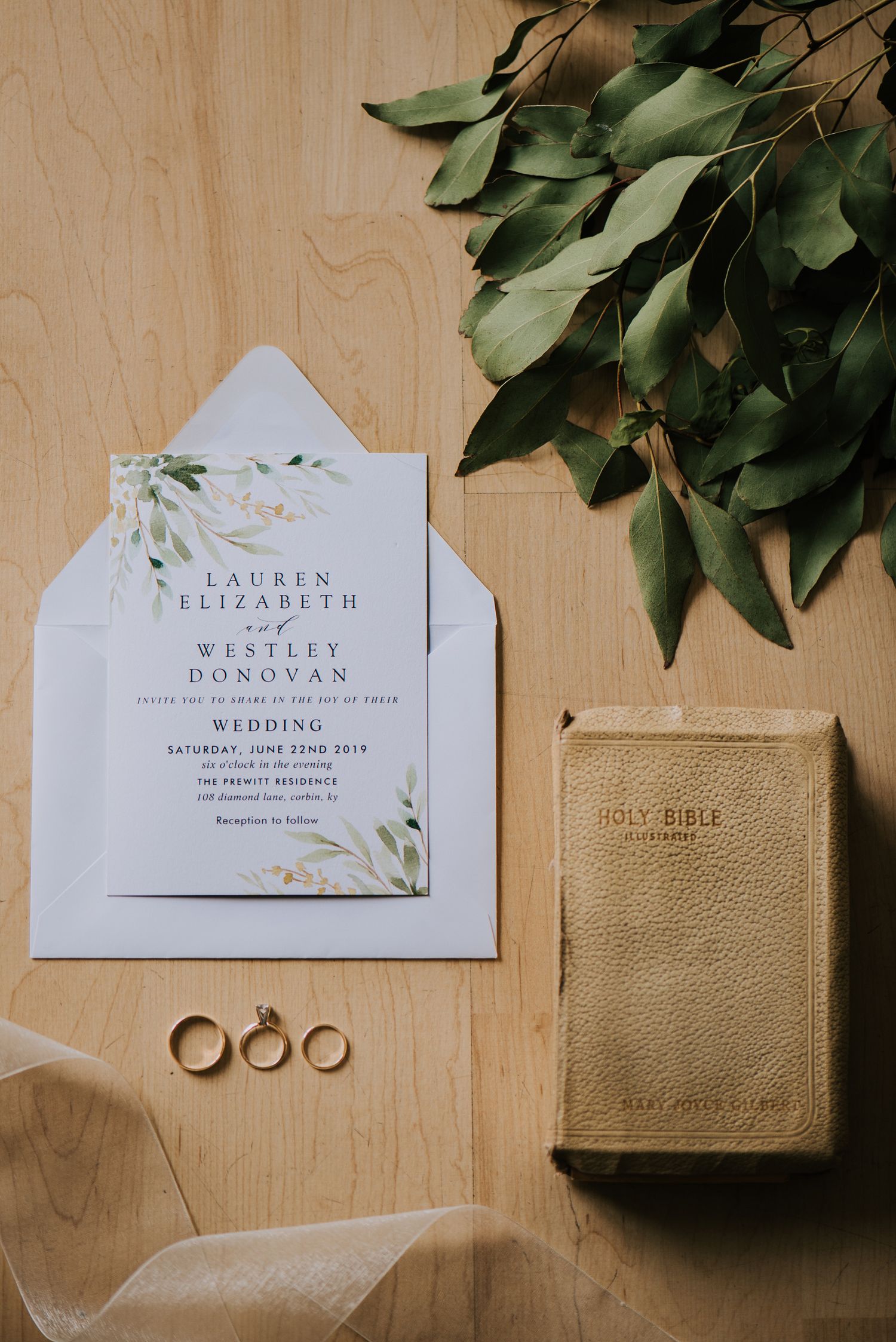 Wedding details including invitations, rings, and a gold Bible on wooden surface.