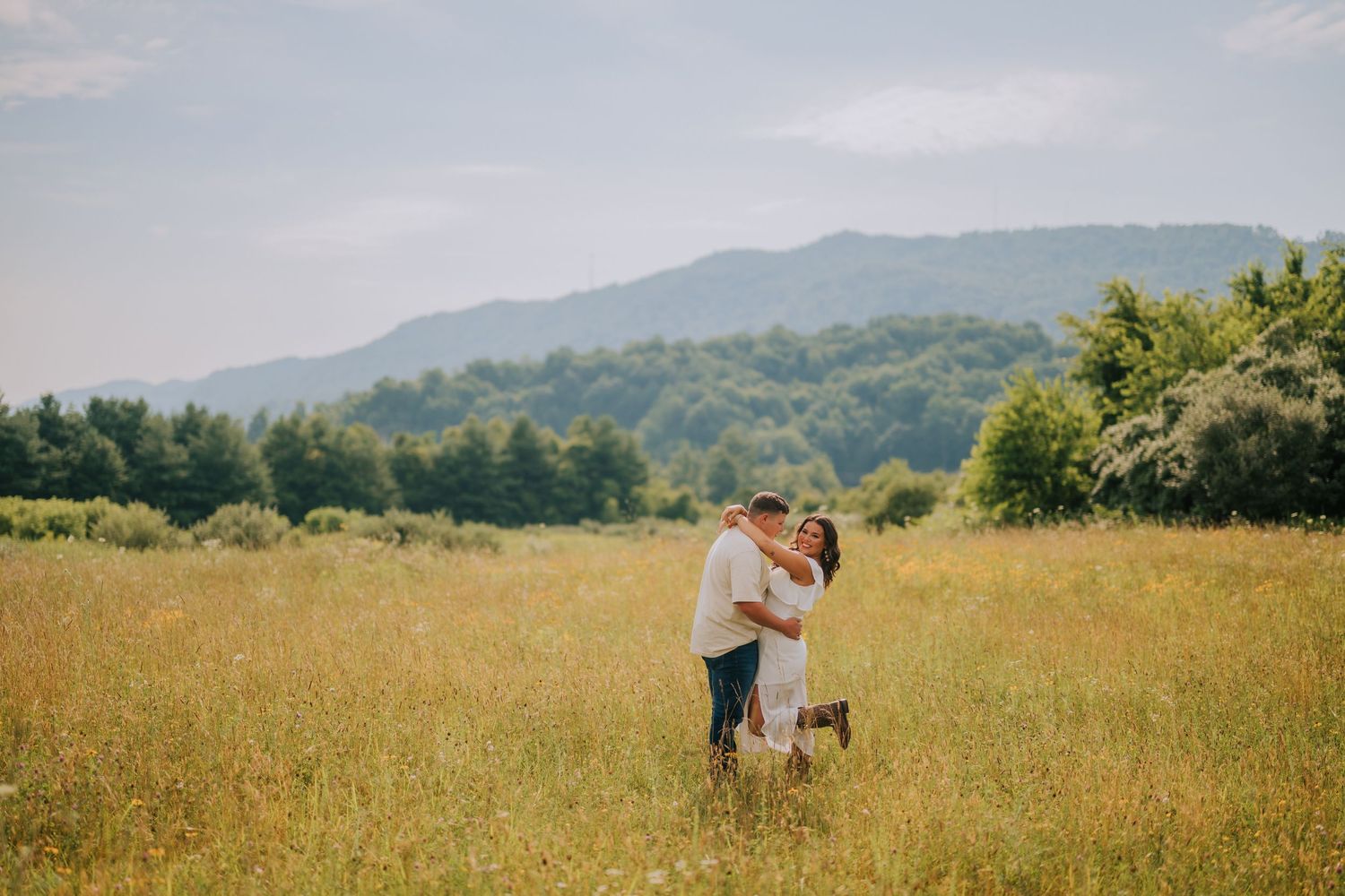 Two people share a tender moment in a golden mountain field on a bright summer day.